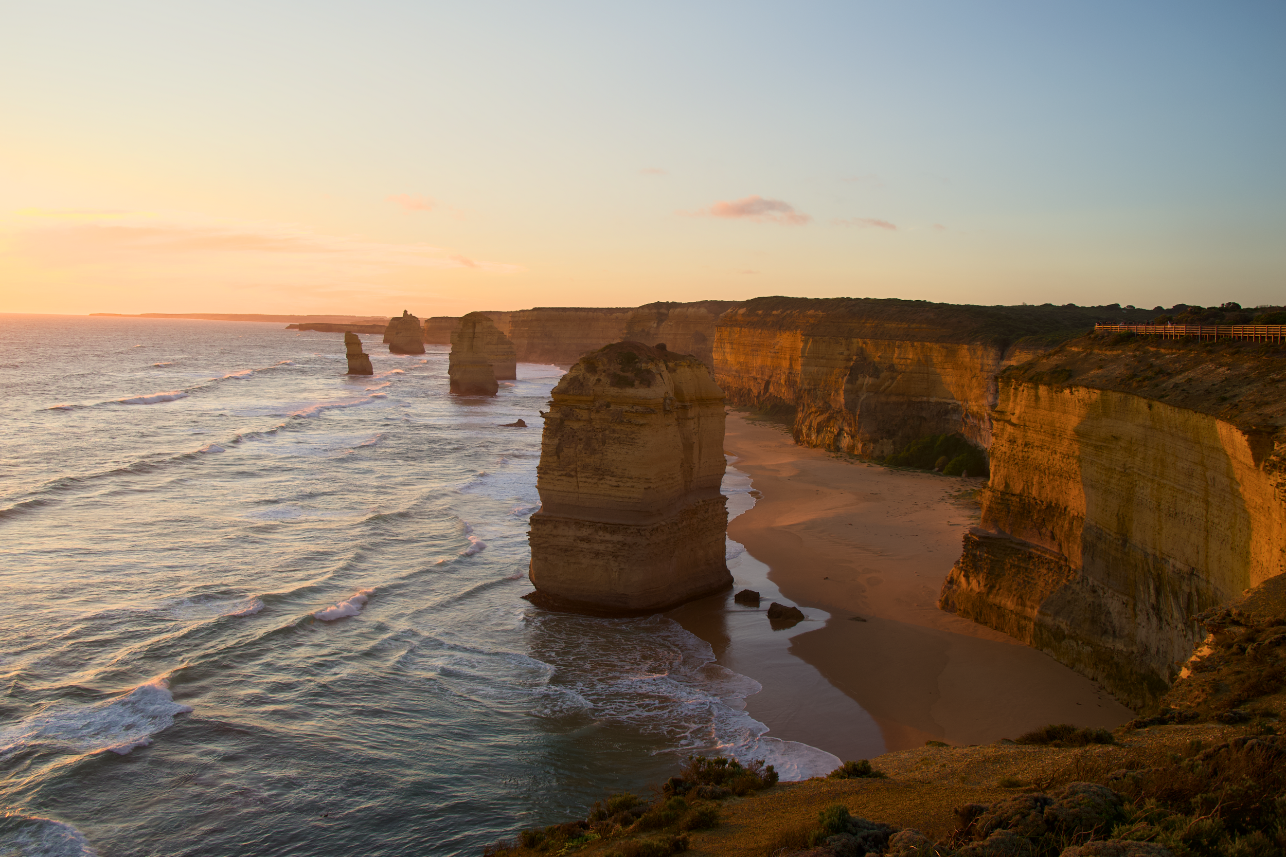 Sunset over the Twelve Apostles limestone stacks along the Great Ocean Road in Australia, with waves crashing on the sandy beach below.