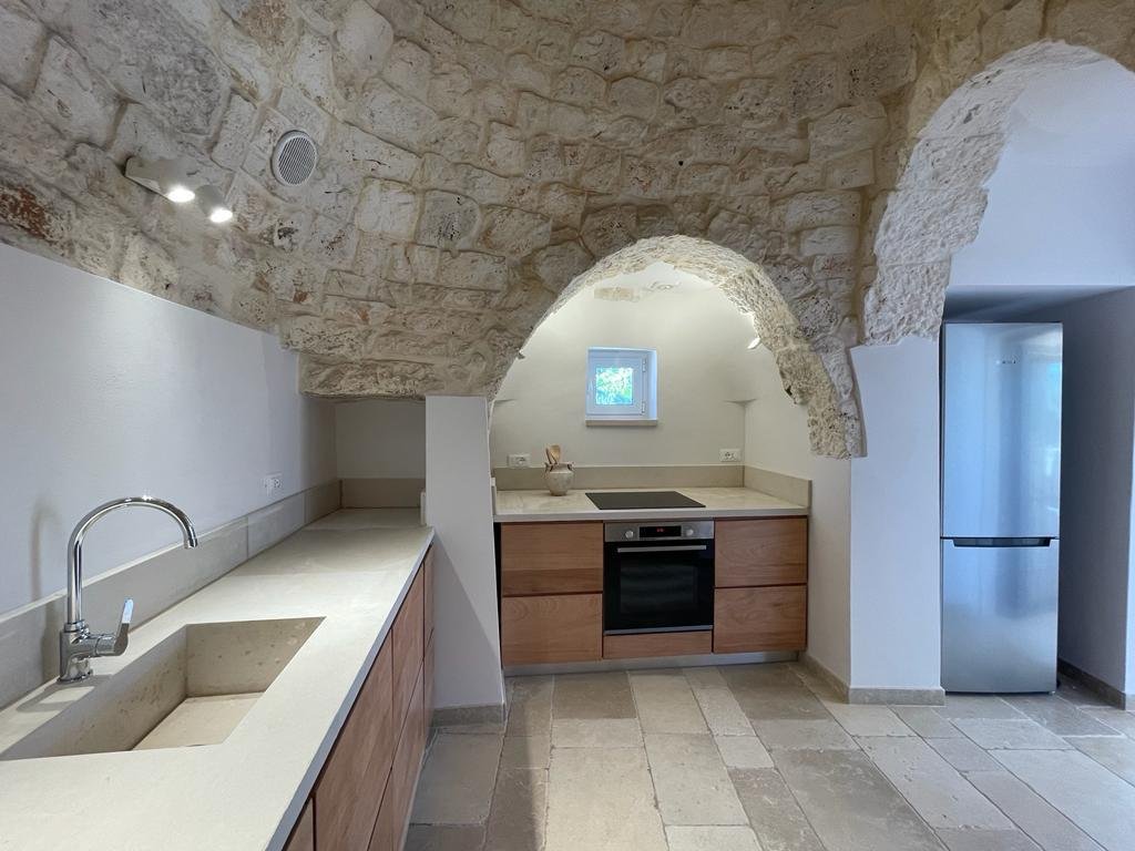 Modern kitchen with stone arch ceiling, built-in oven, stovetop, wooden cabinets, stainless steel fridge, and stone countertops.