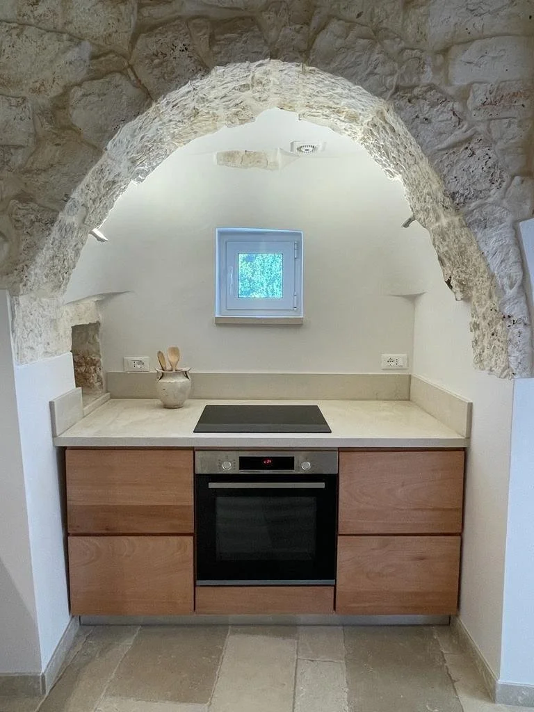 Minimalist kitchen with stone arch, modern stove, and oven under narrow window.
