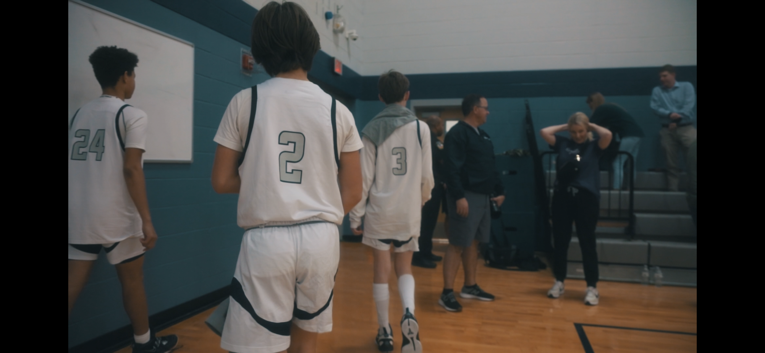 Screenshot from Alex Ervin Hype video for Middle School Basketball game.
Young basketball players in white and black uniforms in a gymnasium, preparing to enter the court after a game.