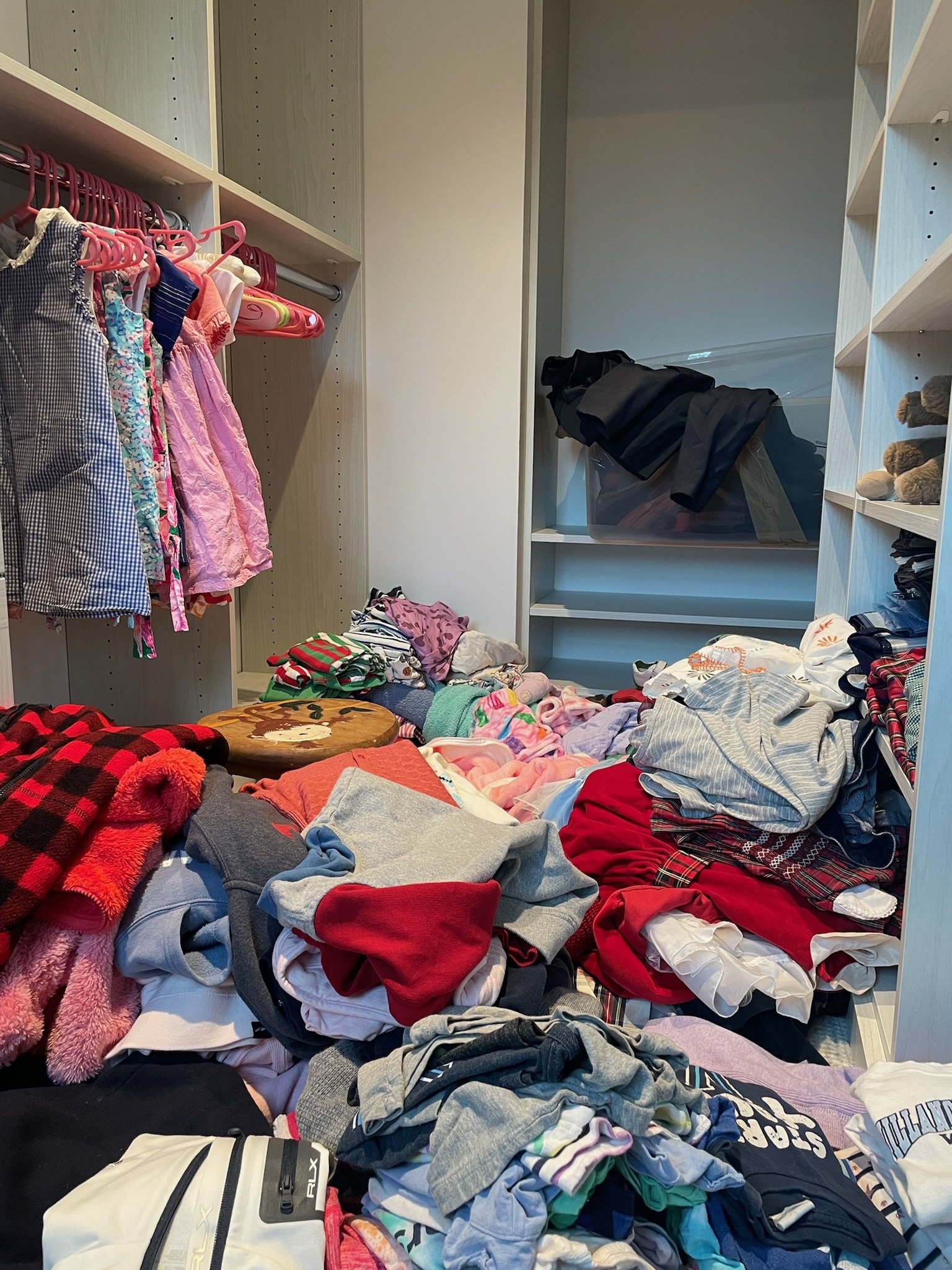 Clothes in disarray on the floor of a closet, with some hanging on a rack and others piled up.