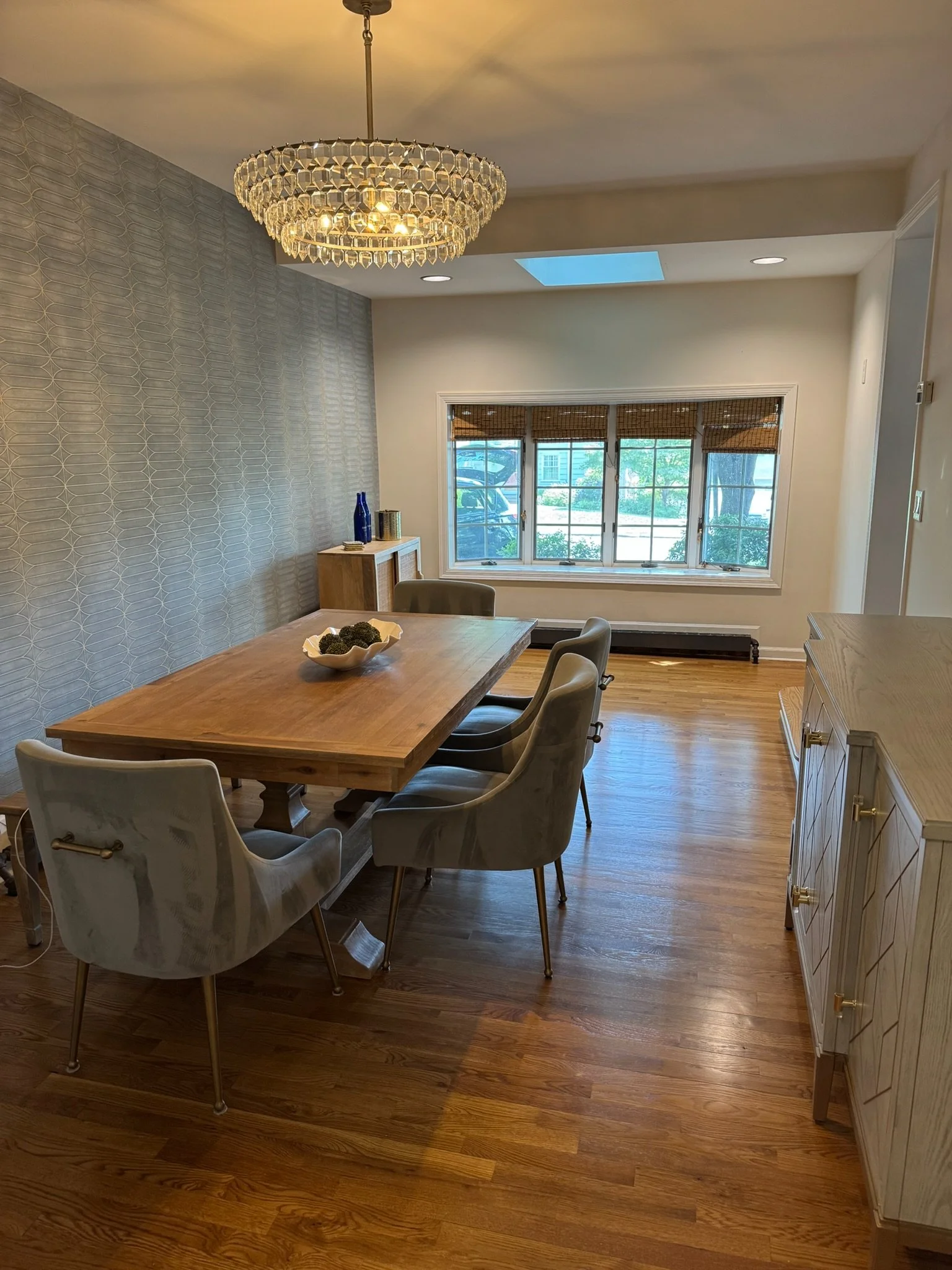 Dining room with a wooden table and six upholstered chairs, a chandelier, a large window, a wooden sideboard, and hardwood flooring.