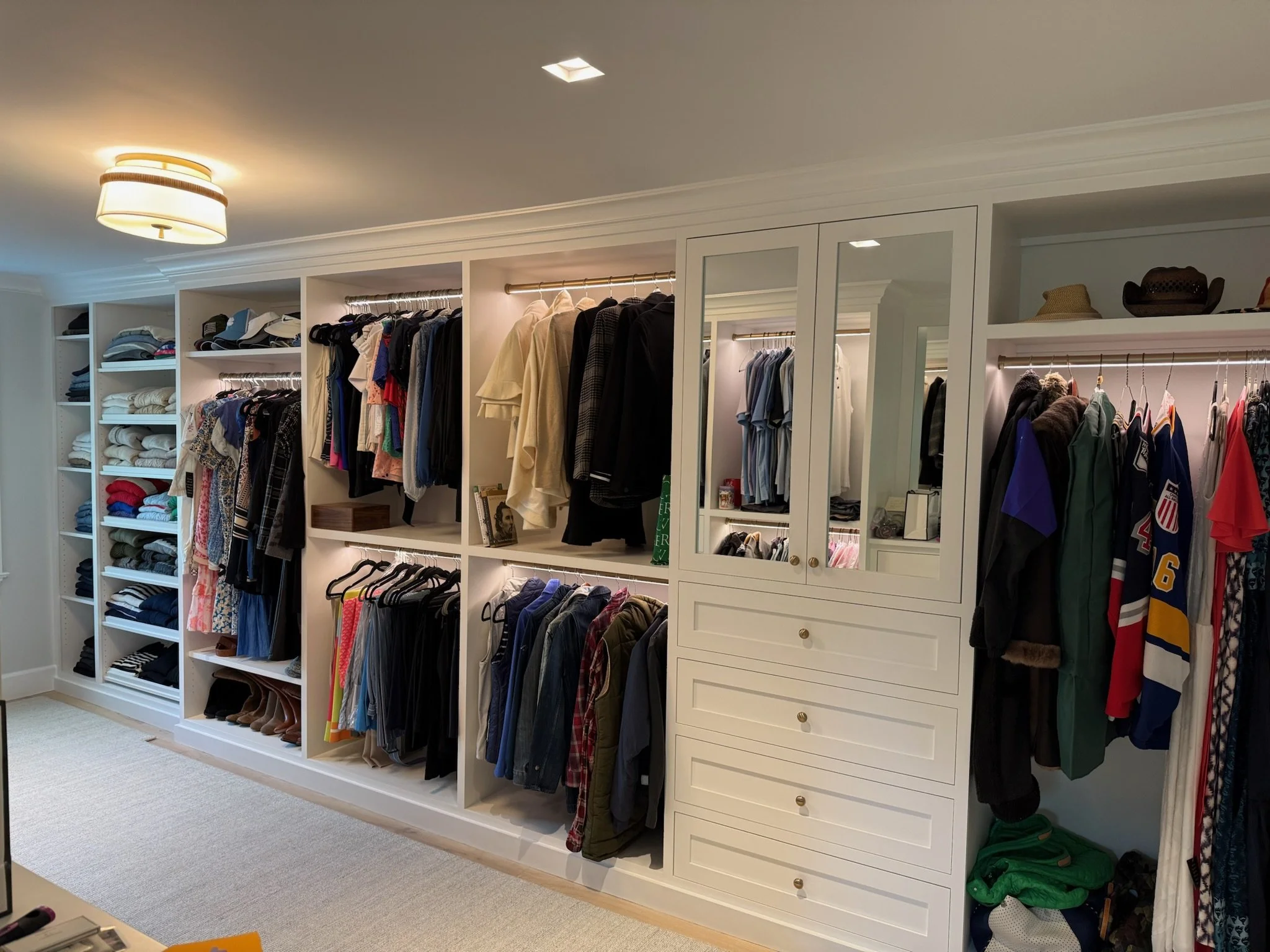 Closet with organized shelves and hanging clothes, including shirts, jackets, pants, and sports jerseys, with some hats on top.