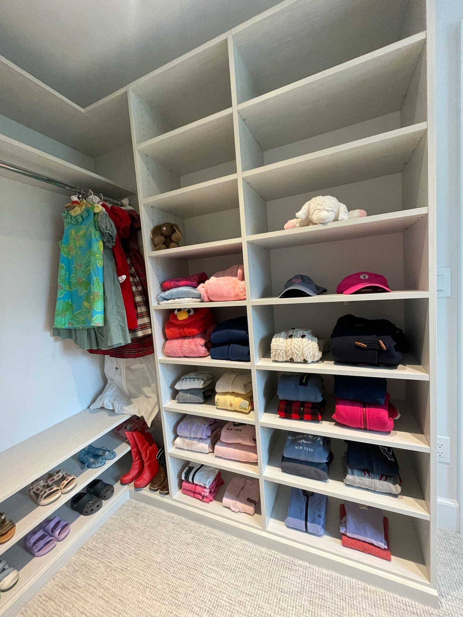 A closet with multiple shelves filled with folded clothes and hats, and a hanging rod with colorful dresses.