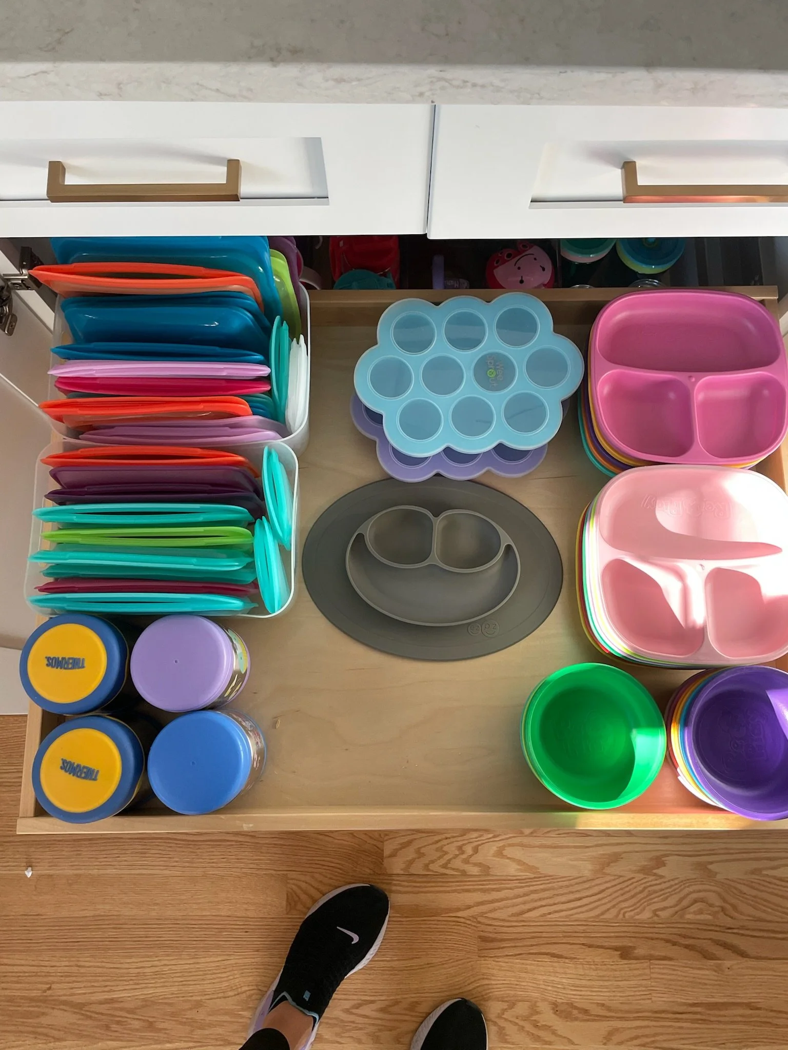 Child's drawer containing colorful plastic plates, bowls, and containers for food or snacks.