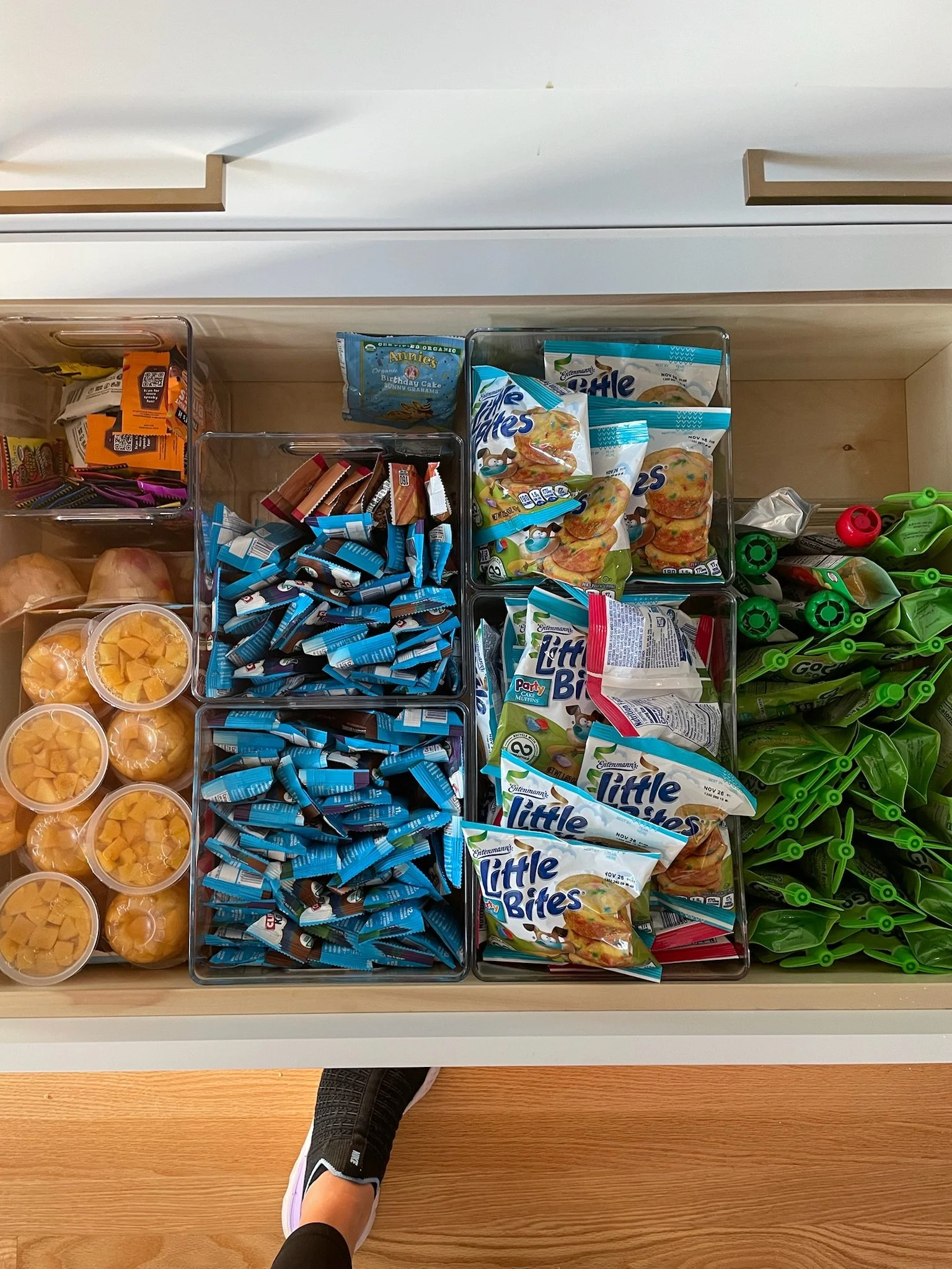 Open drawer filled with various snack packets and containers, including Little Bites snack bags, fruit cups, and chips, organized in compartments.