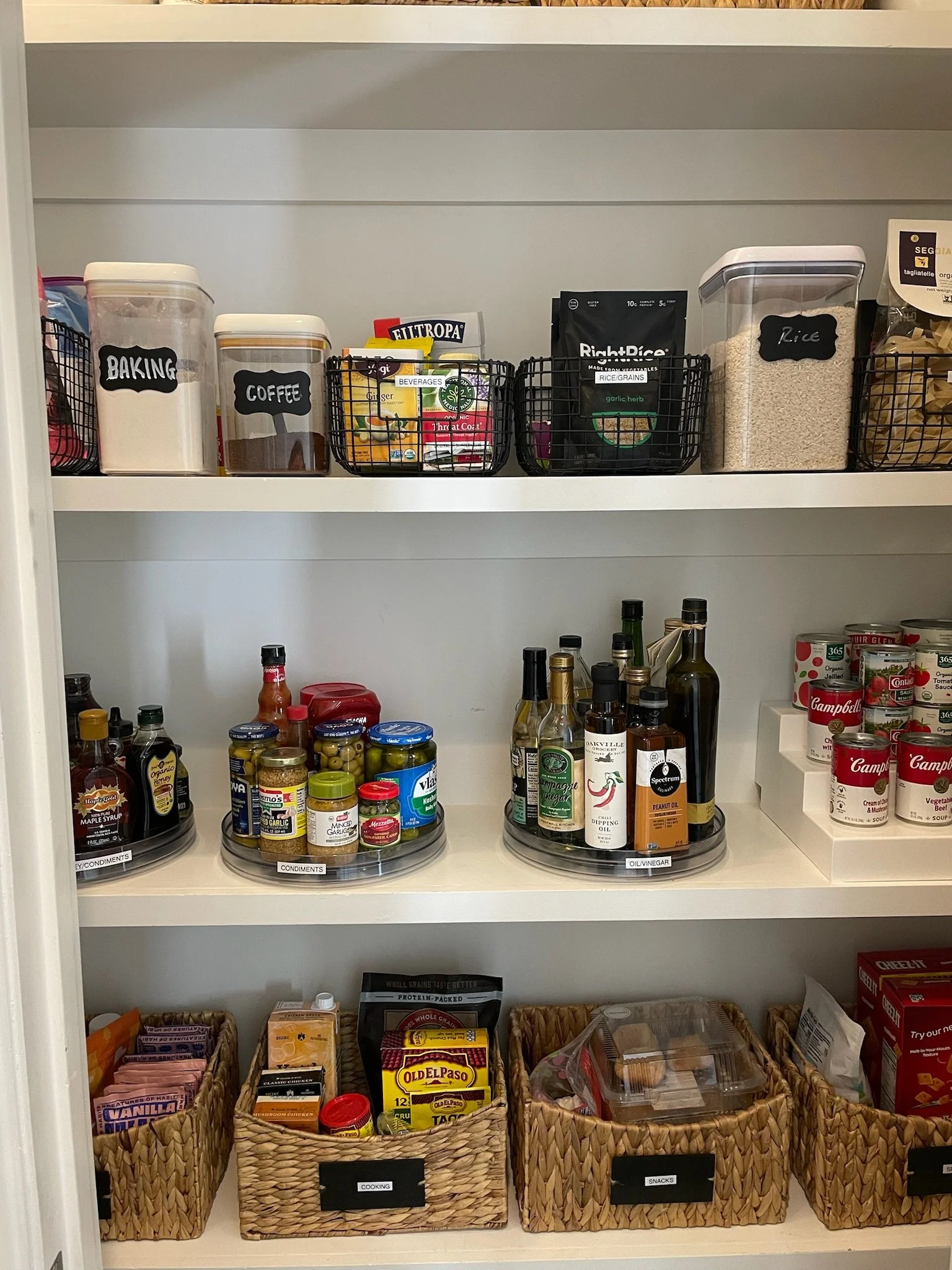 Pantry shelf with labeled containers, jars, bottles, and baskets of snacks and cooking supplies.