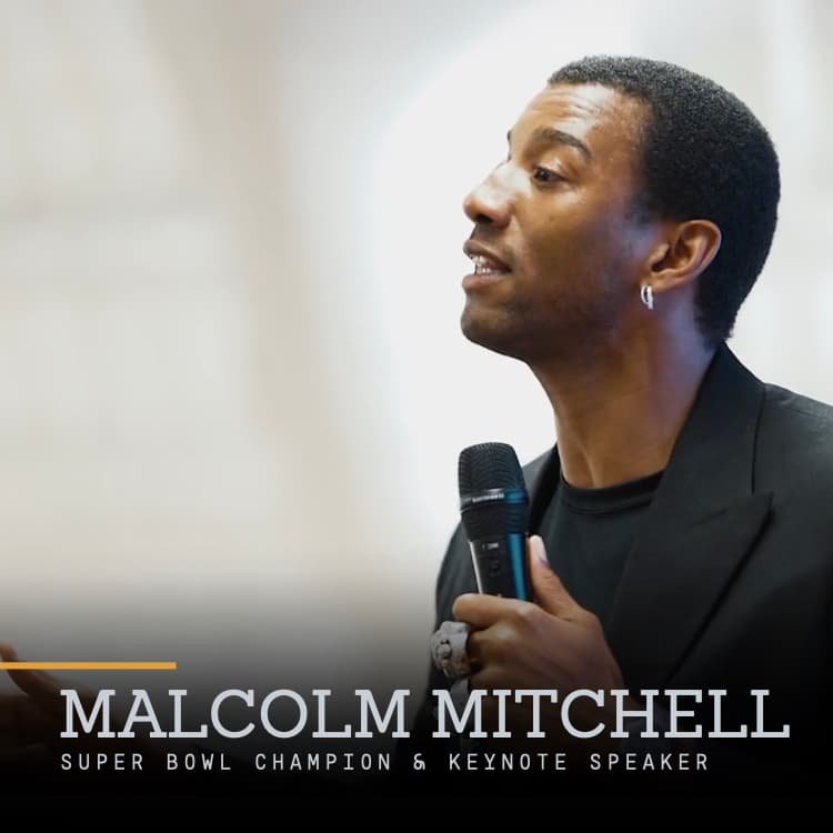 Malcolm Mitchell speaking into a microphone, wearing a black blazer and black shirt, with text overlay 'Malcolm Mitchell Super Bowl Champion & Keynote Speaker'.