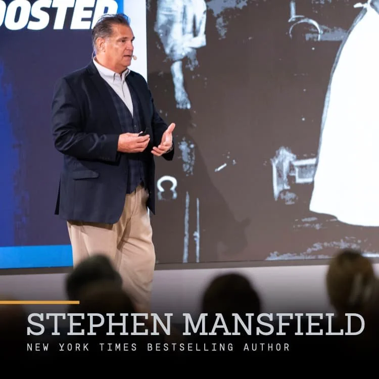 Stephen Mansfield speaking at a conference with a large screen behind him displaying a black and white image. The bottom text reads "Stephen Mansfield, New York Times Bestselling Author."