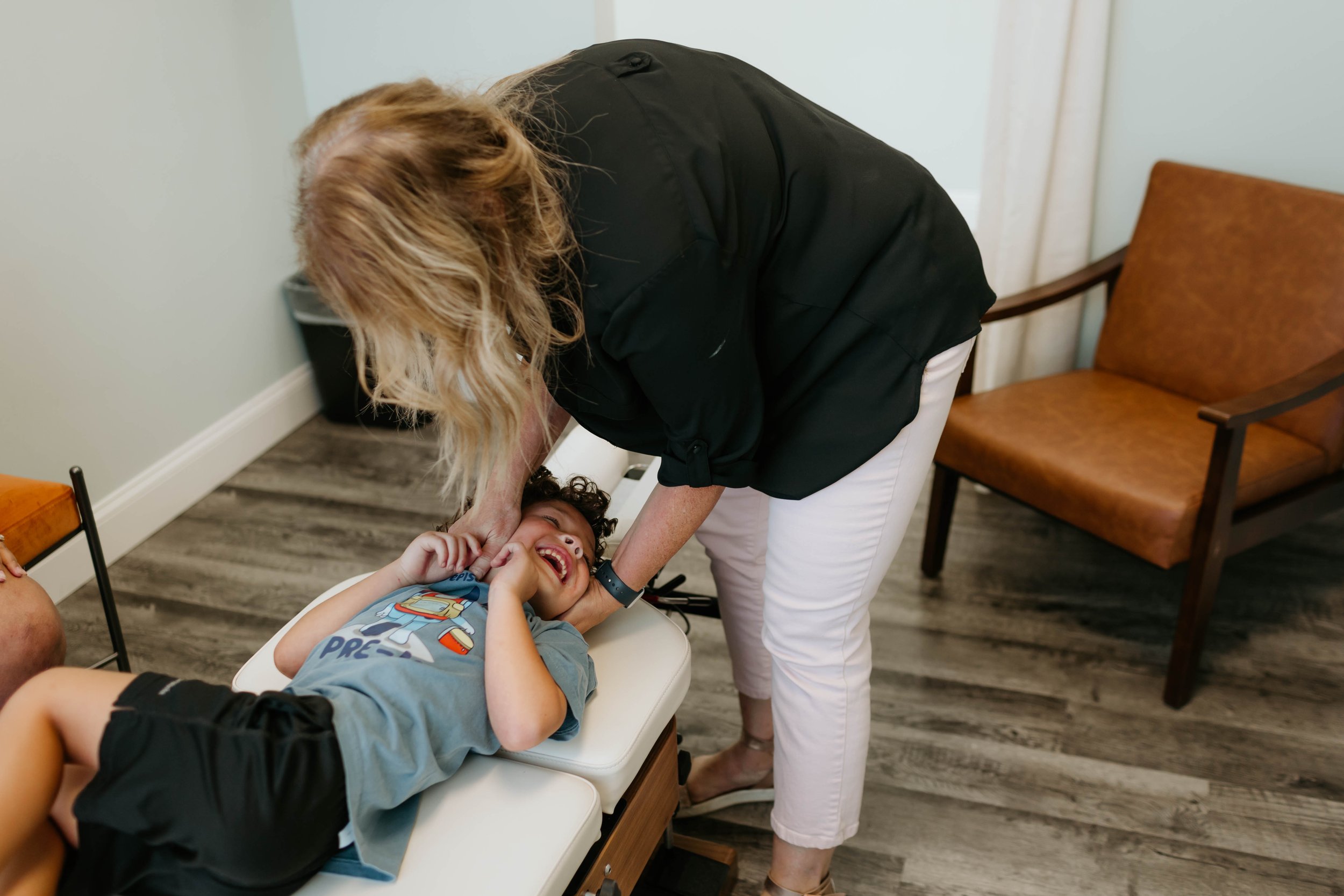 Dr. Stephanee Lewis performing a gentle pediatric chiropractic adjustment on a laughing child at Thrive Family Chiropractic in Montgomery AL