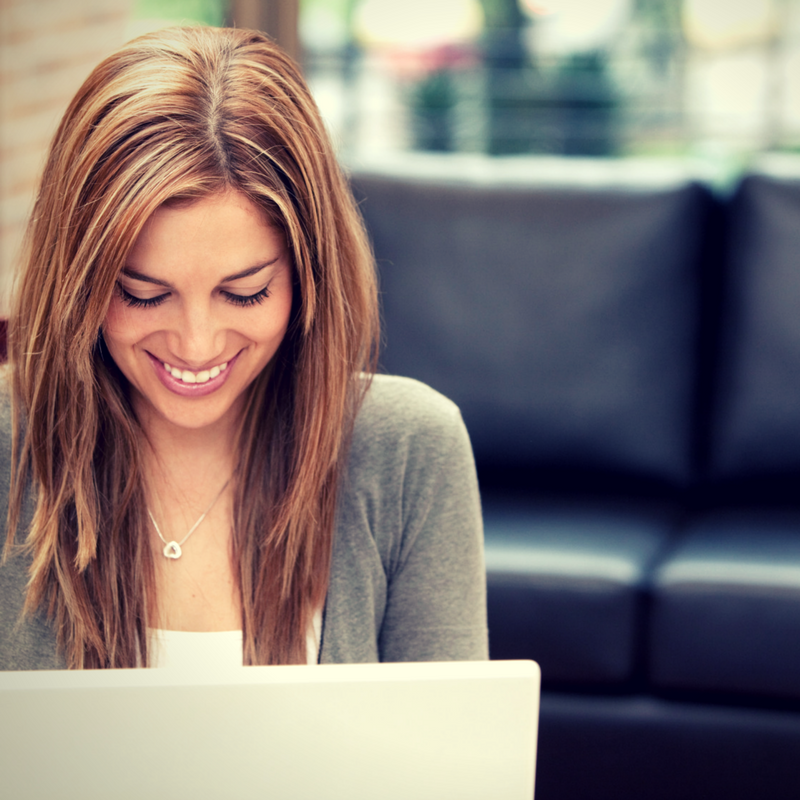 Young woman smiling while looking at laptop in modern living room.
