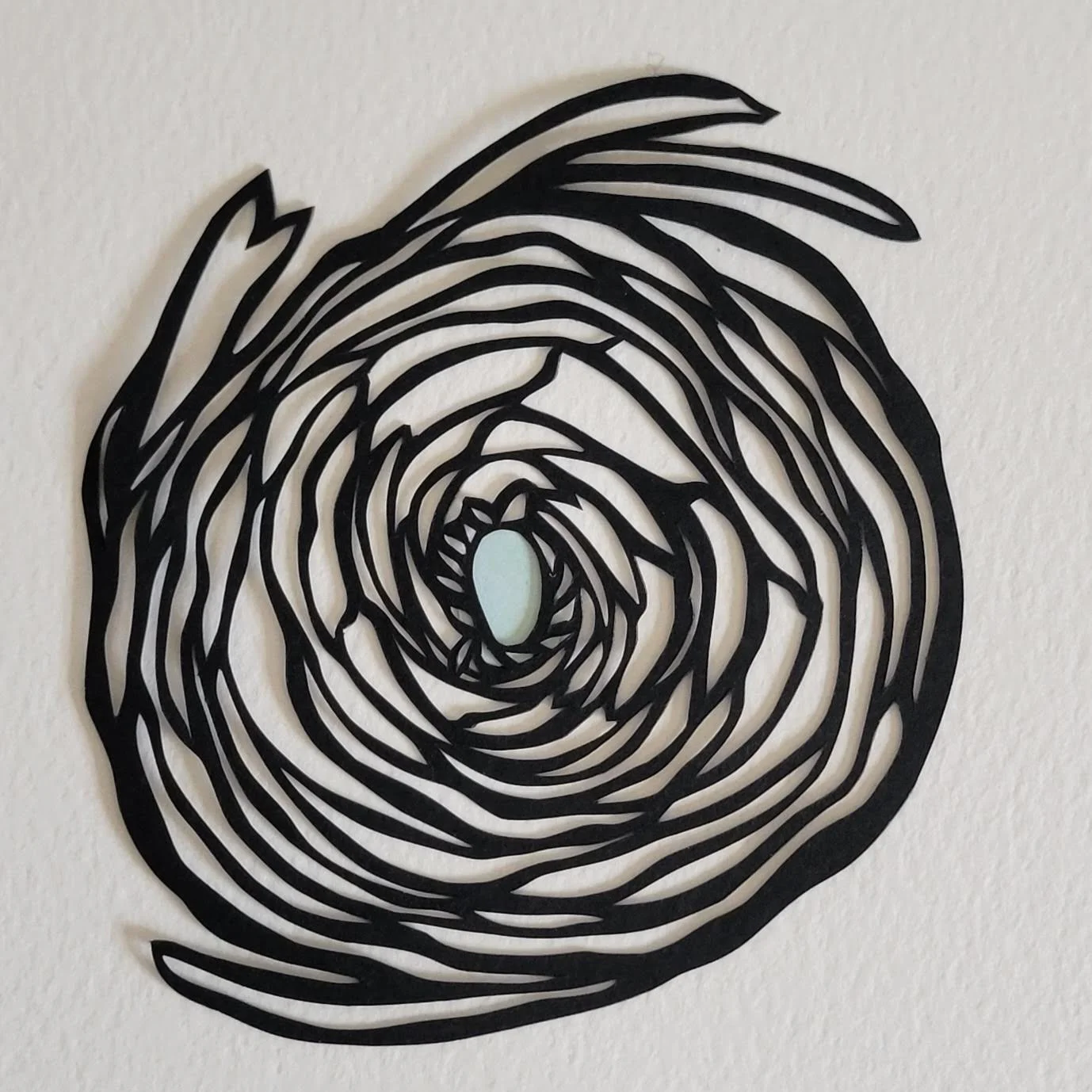 A papercut nest in black and white with a tiny blue egg in the middle of the nest