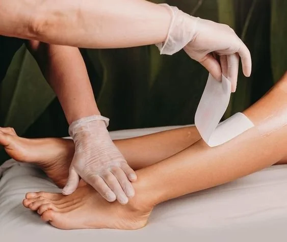 Someone applying wax to a person's leg for hair removal with a cloth strip in a beauty salon.