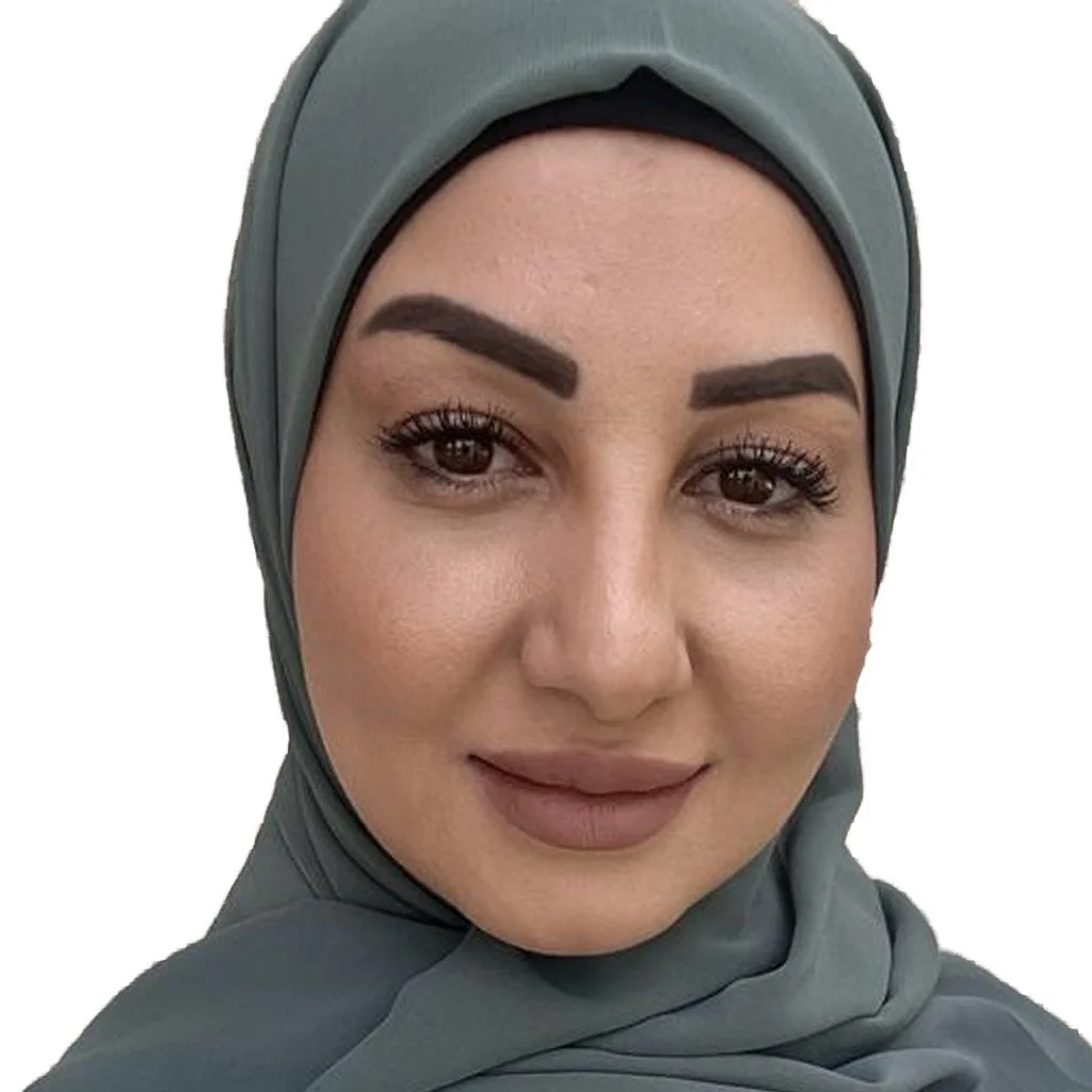 Close-up portrait of a woman wearing a gray hijab, smiling softly, with makeup including dark eyebrows, eyeliner, and nude lipstick.