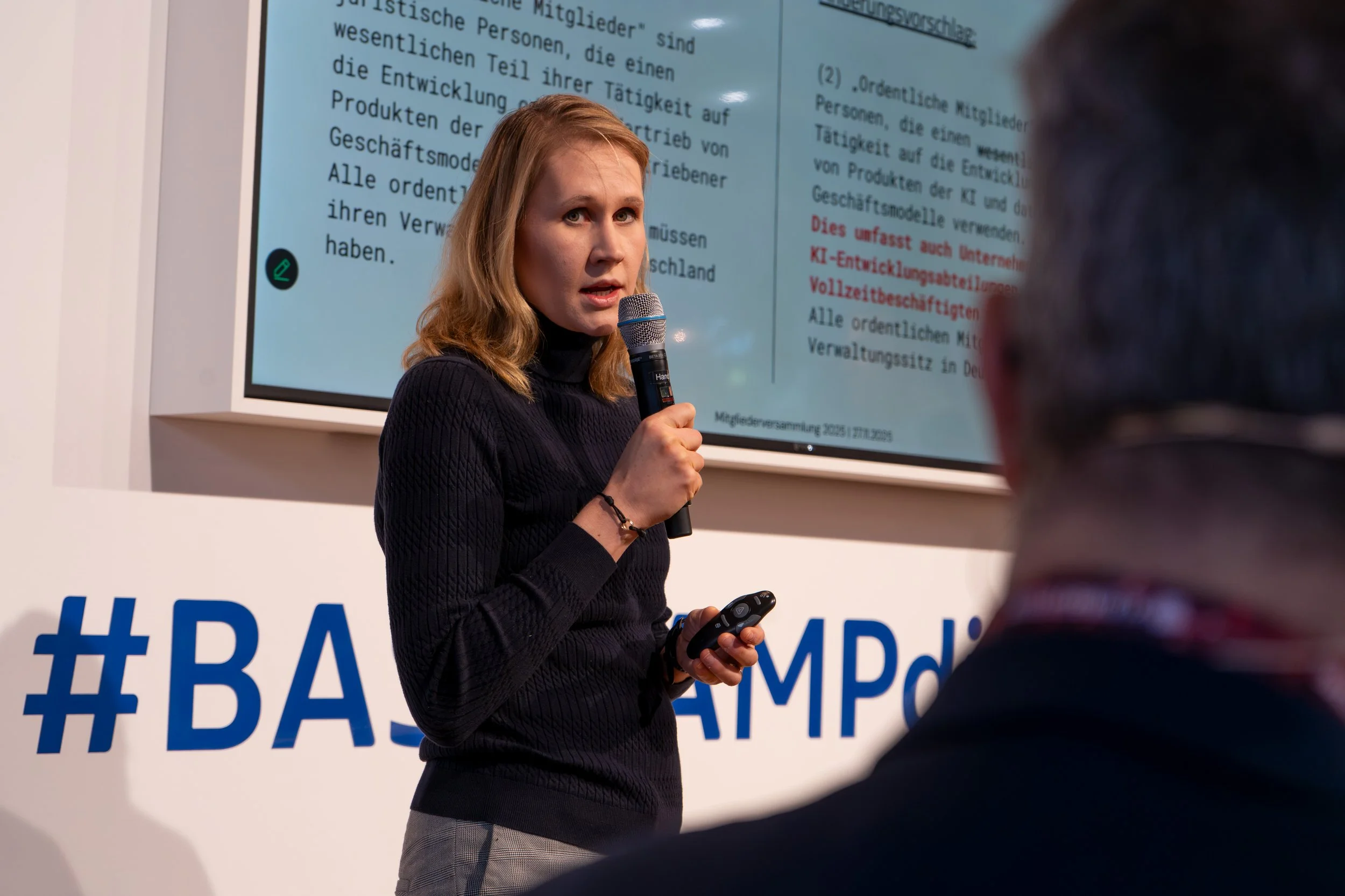 Dr. Vanessa Just steht auf der Bühne vor einem großen, digitalen Hintergrund. Sie spricht ins Mikro.