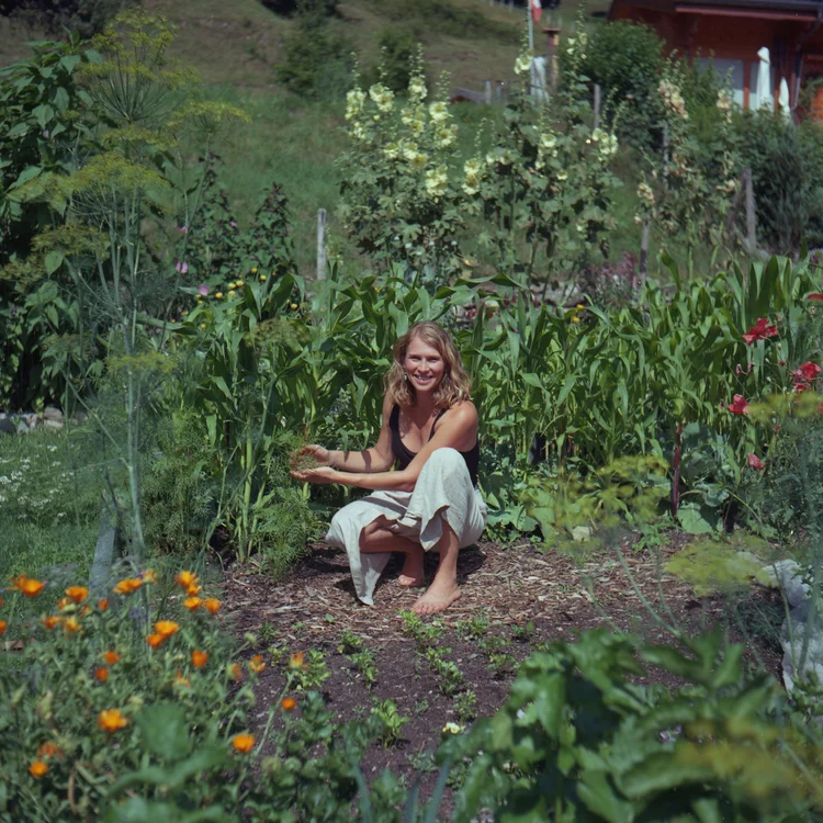 Sonia sitting among the vegetable beds and flowers of her mountain garden