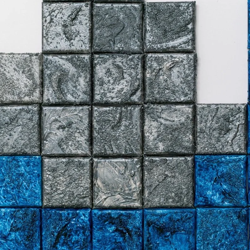 Close-up of textured square tiles in gray, white, and blue colors arranged in a pattern.