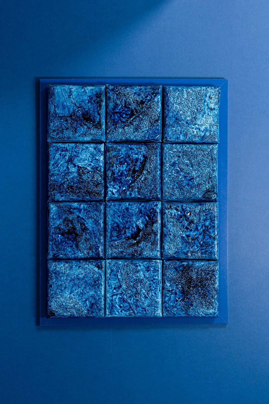 Abstract blue textured artwork with nine square panels mounted on a wall.