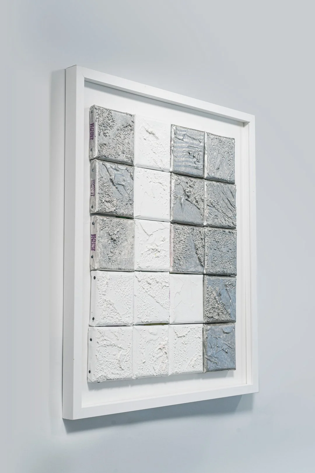 A framed display of 16 textured tile samples arranged in a 4x4 grid on a wall.