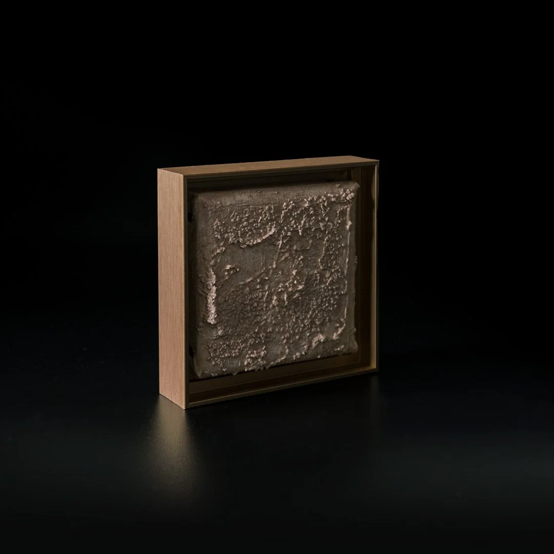A framed piece of textured, rough gray material or artwork displayed on a black background.
