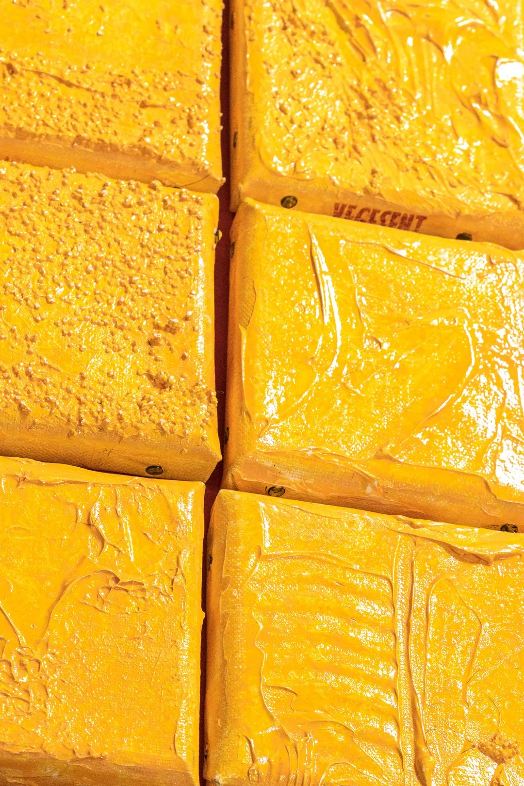 Several blocks of yellow cheese, some with textured or smooth surface, stacked closely together.