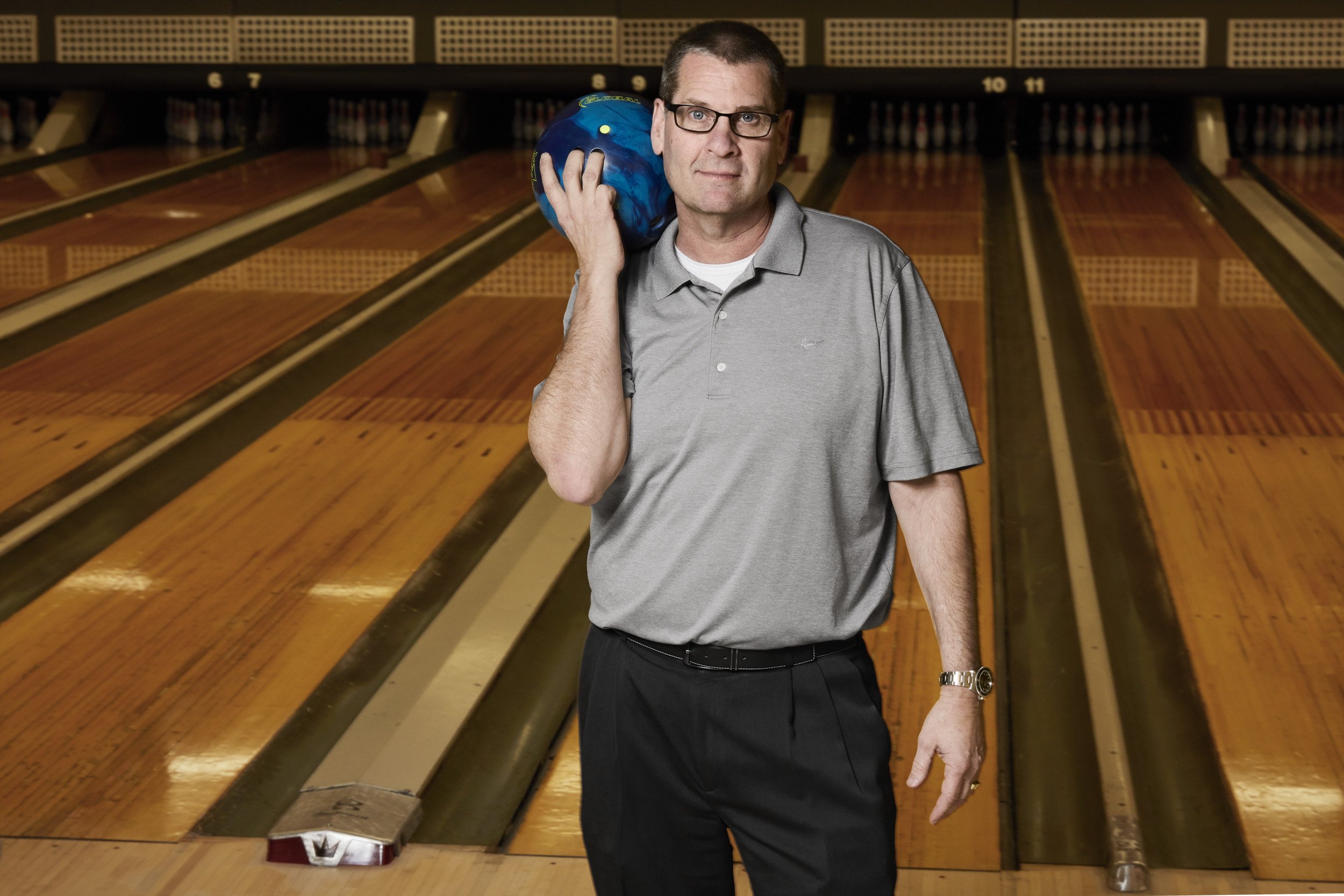 man holding bowling ball with bowling alley behind him