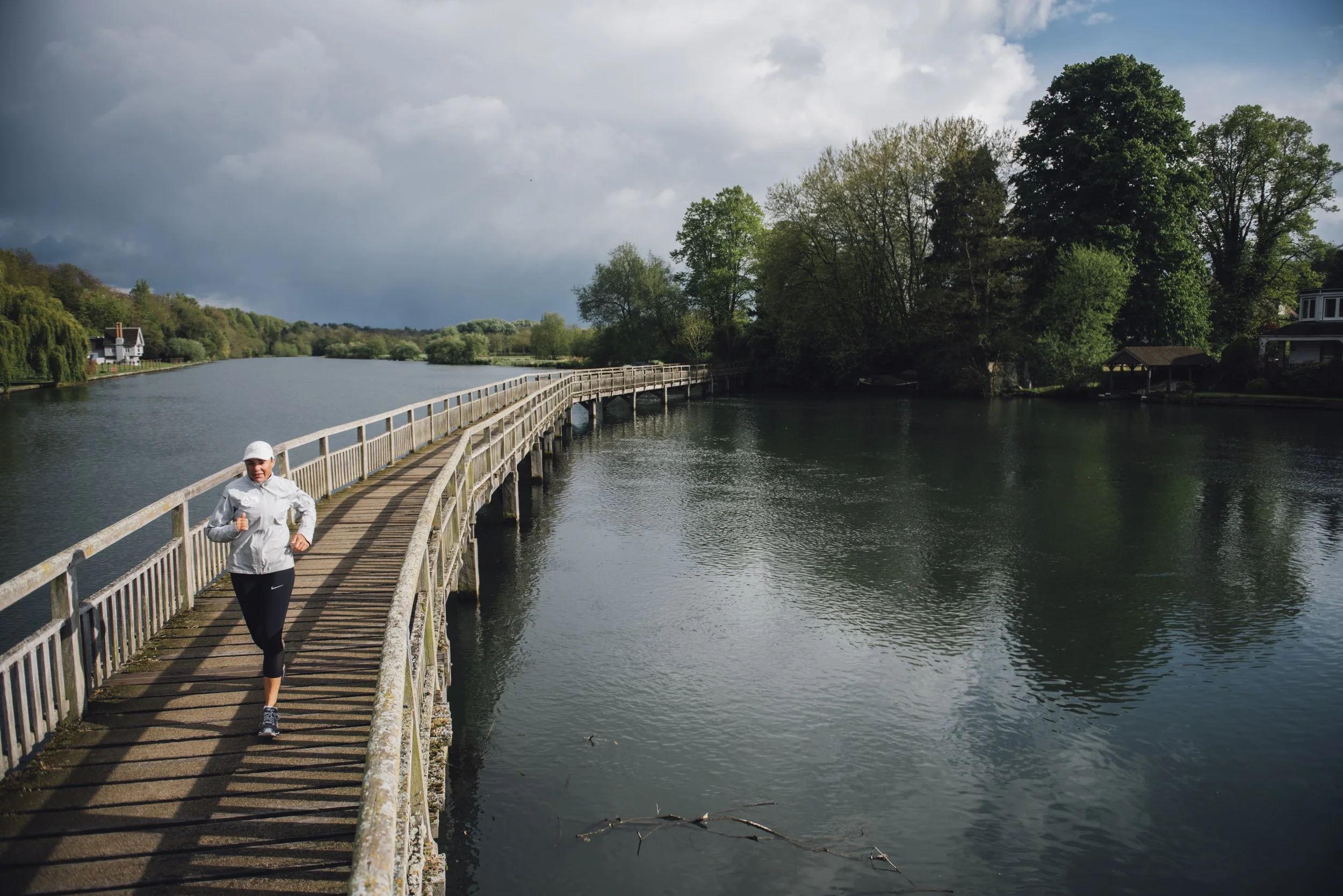 Person jogging on a wooden bridge over a river surrounded by trees.