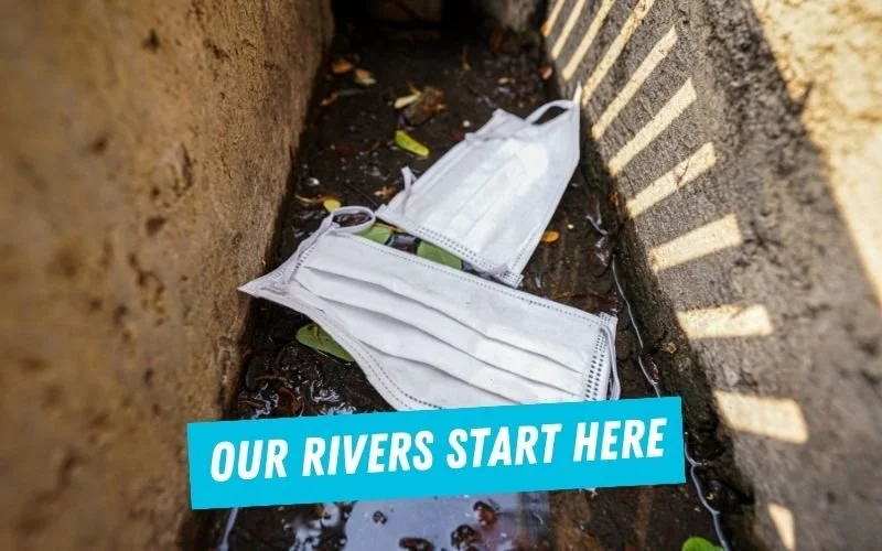 Disposable face masks littered in a water drain, with text 'Our rivers start here.'
