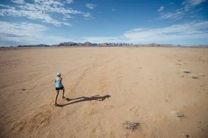 Lone person running in vast desert landscape under blue sky