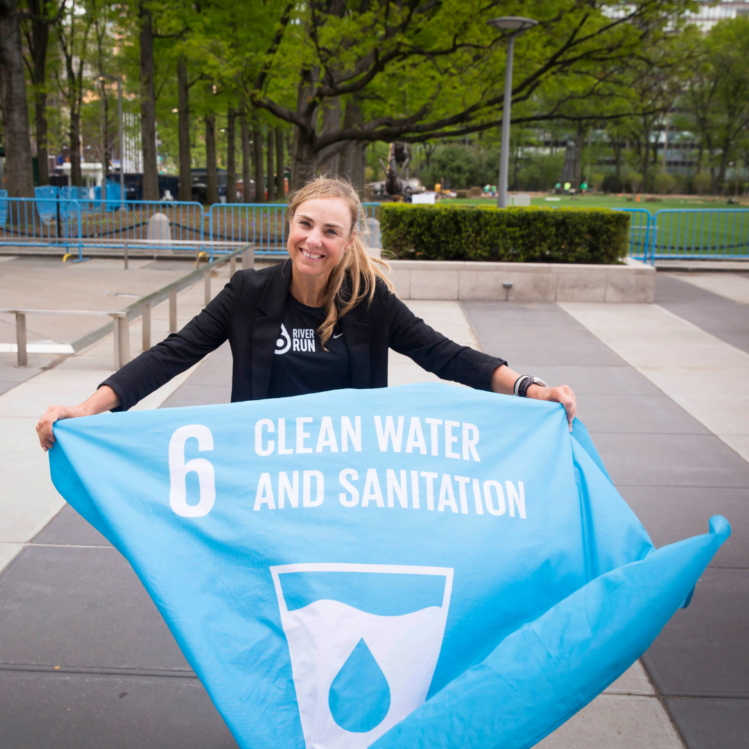 Person holding a banner promoting clean water and sanitation, outdoor setting with trees and pathways in the background.