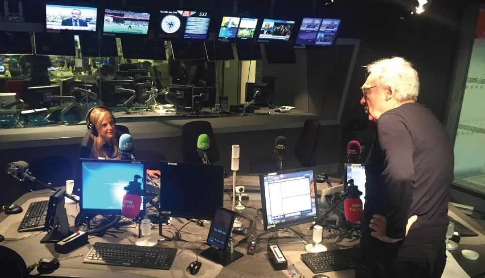 Radio studio with two people, microphones, and multiple monitors.