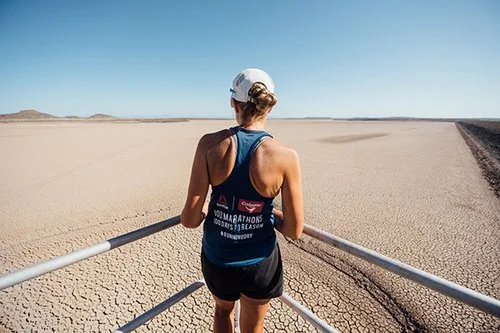 Person in running attire standing on a platform overlooking a vast, dry, cracked landscape.
