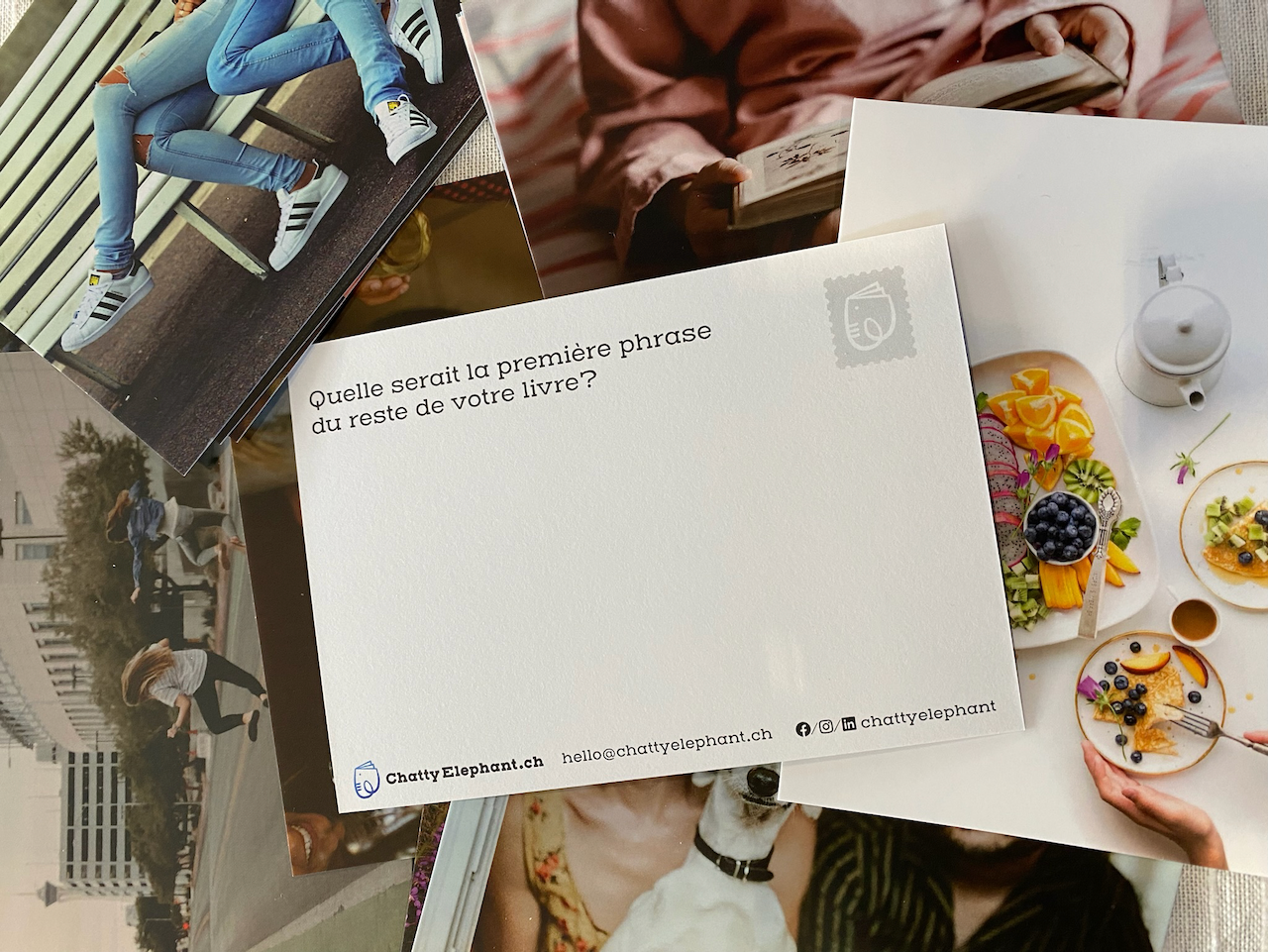 Une carte postale posée sur un plateau avec des fruits, des pancakes décorés et une théière, entourée de photographies de personnes en plein air.