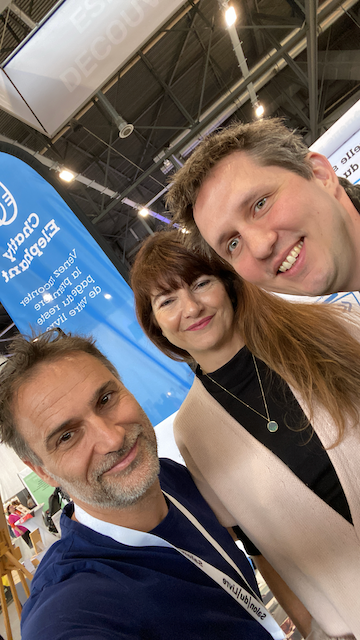 Trois personnes posent pour une selfie dans un environnement d'exposition ou de salon.