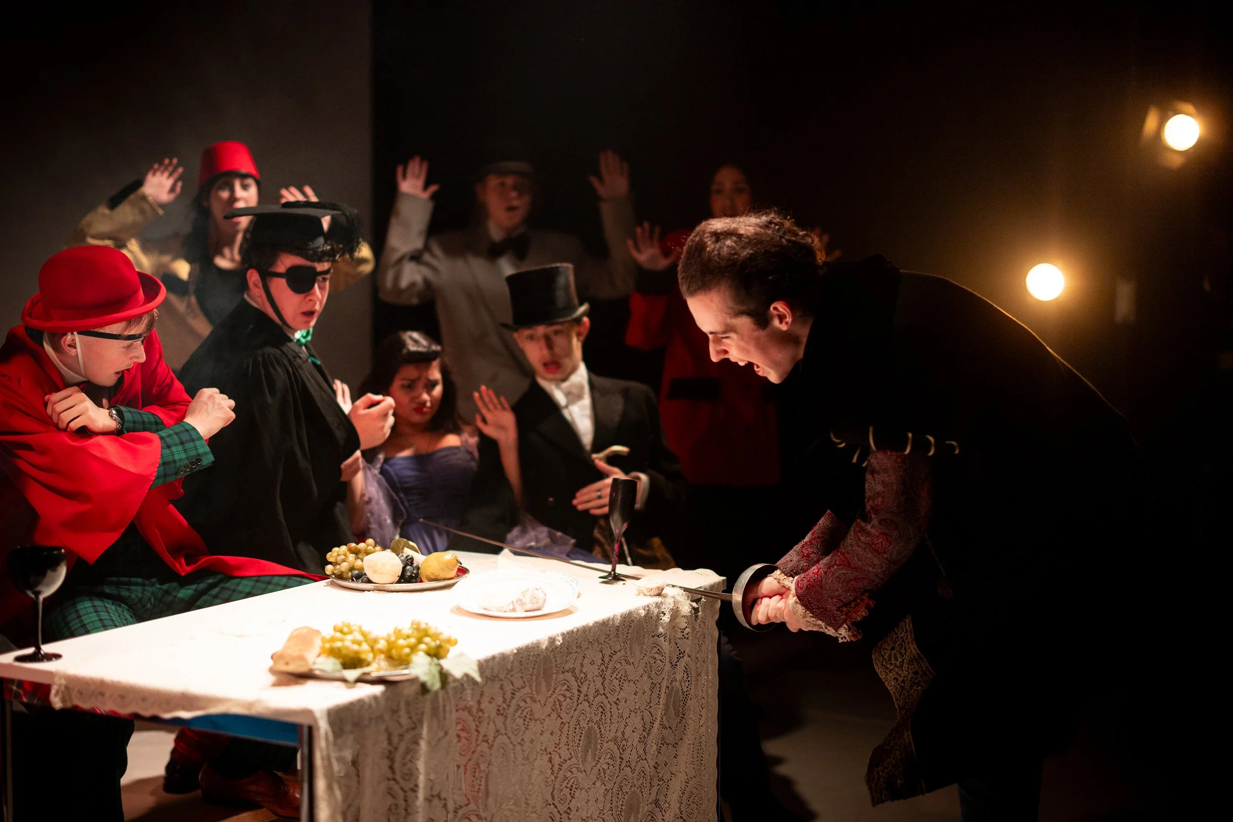 People dressed in costumes around a table with food, engaging in a theatrical performance or skit.