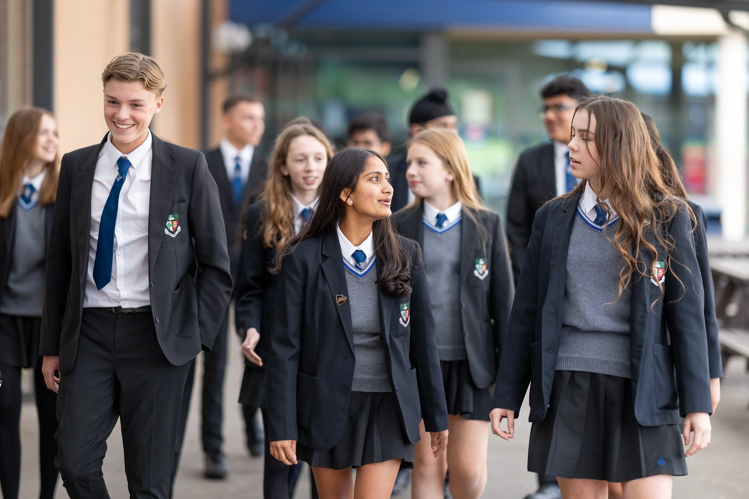 Group of students in school uniform walking outdoors, engaged in conversation and smiling.