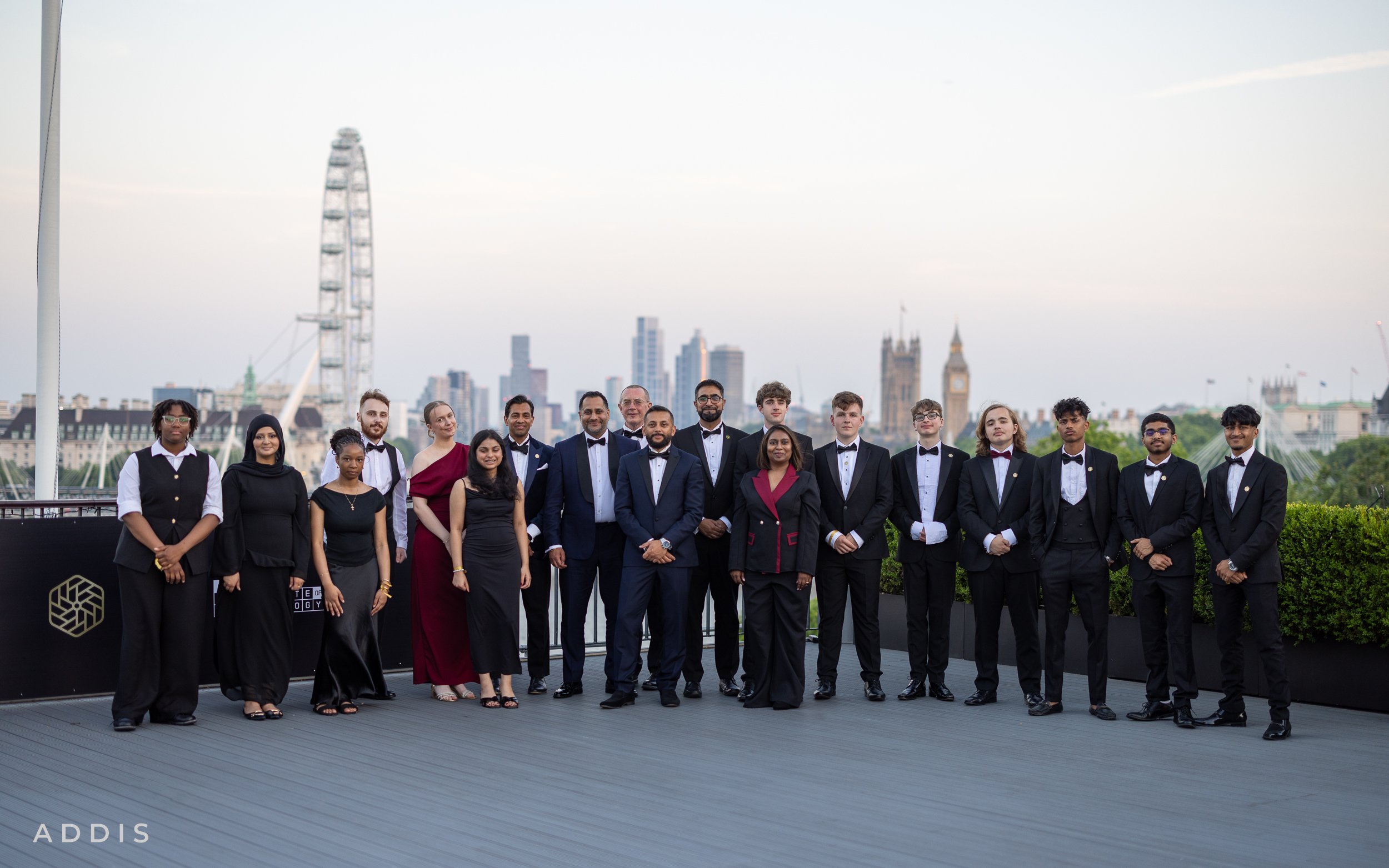 Group of diverse people at the National Innovation Challenge Awards at the IET in formal attire standing outdoors on a terrace with cityscape background, including London landmarks like Big Ben and the London Eye.
