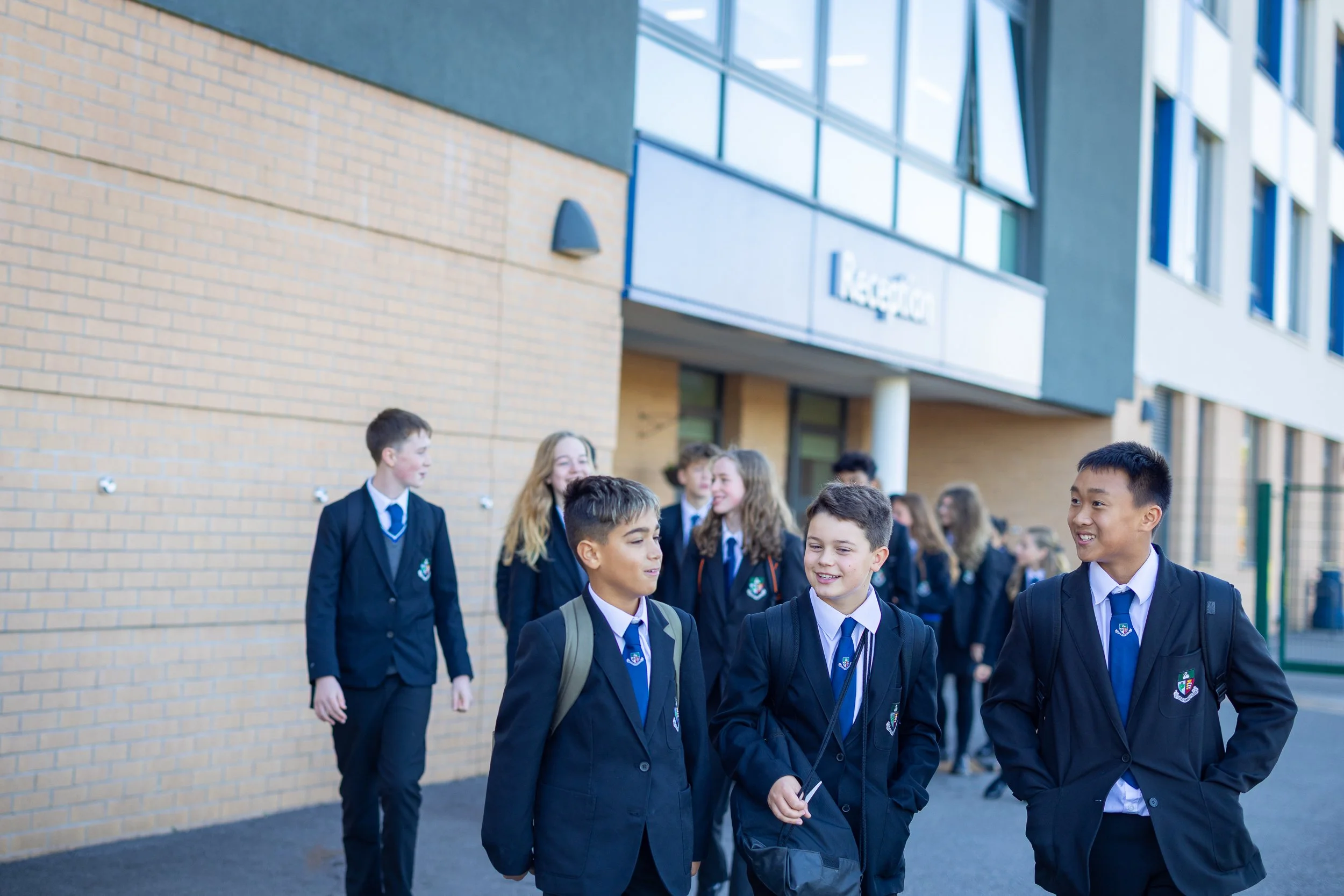 Students in school uniforms standing and talking outside a school building.