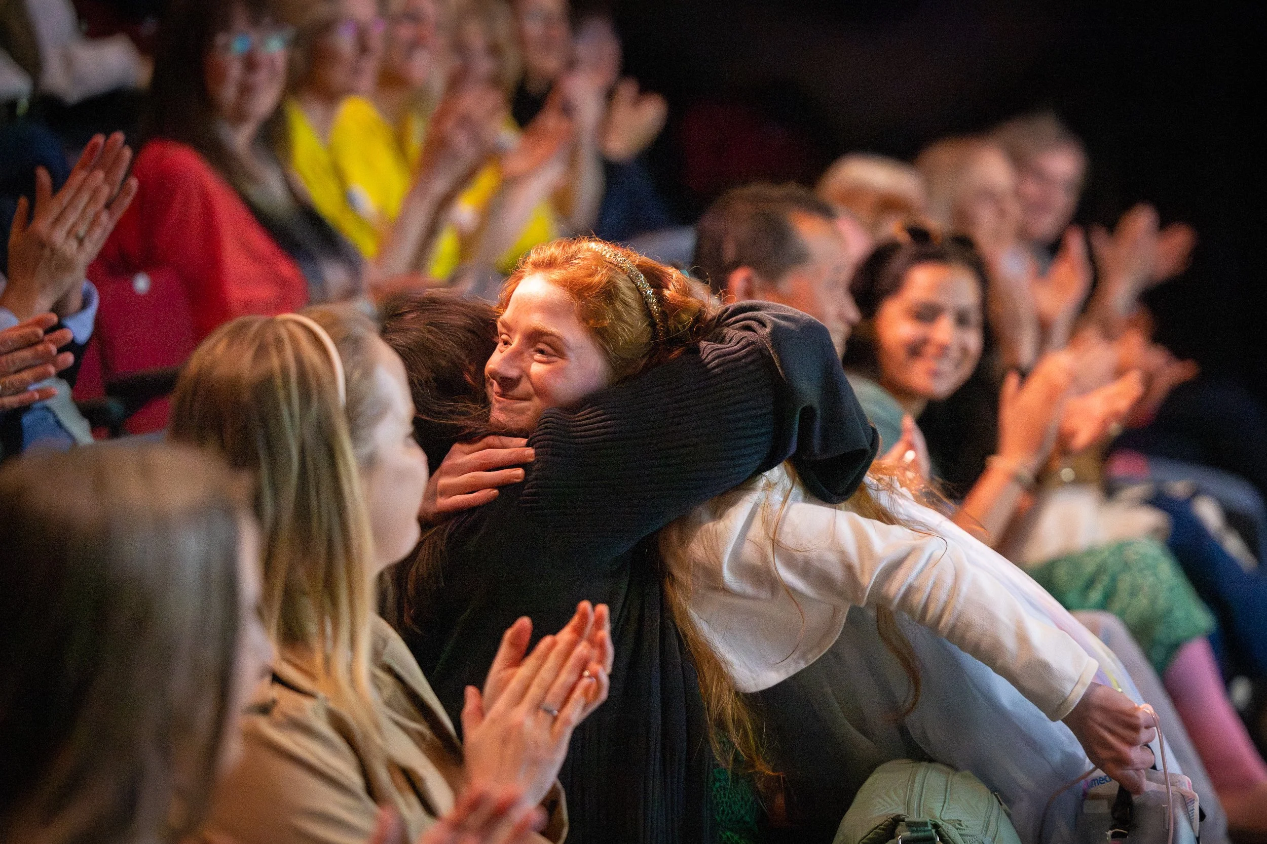People sitting in an audience, clapping and smiling during a OneRichmond charity event congratulating a singer who performed.