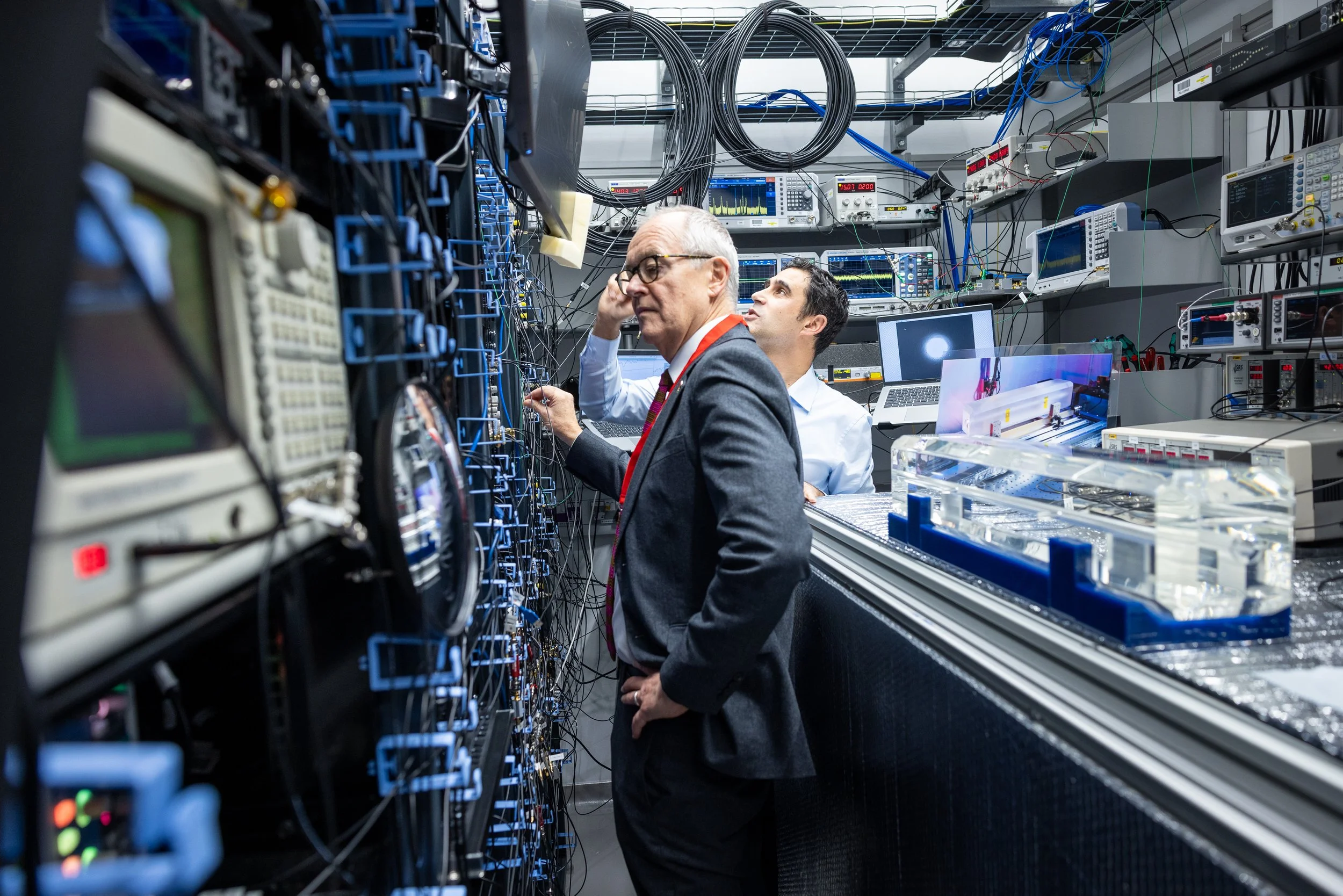 Lord Vallance and a scientist working in a high-tech server room filled with computer hardware, cables, and monitors.