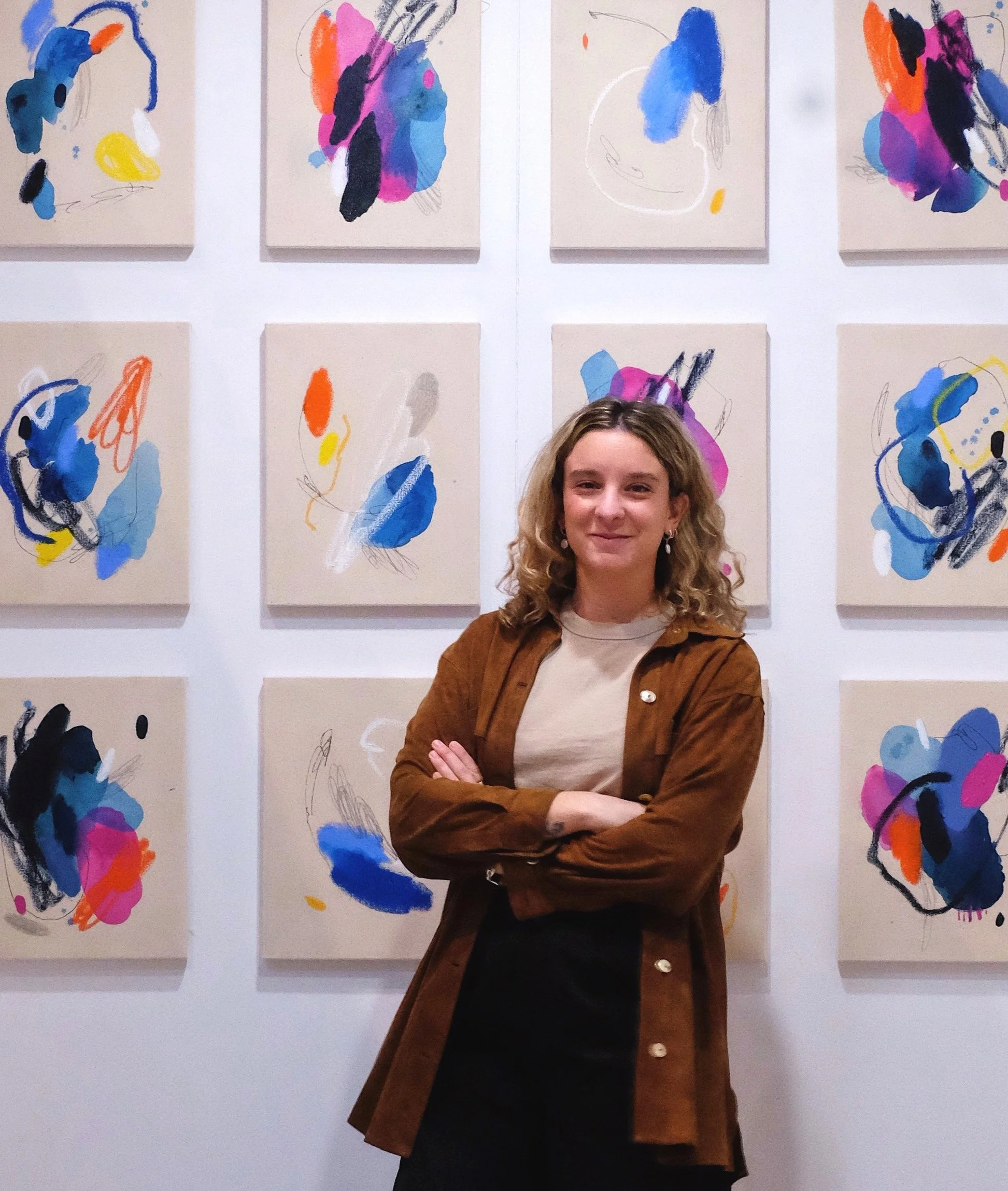 Persona frente a una pared con nueve cuadros abstractos coloridos.