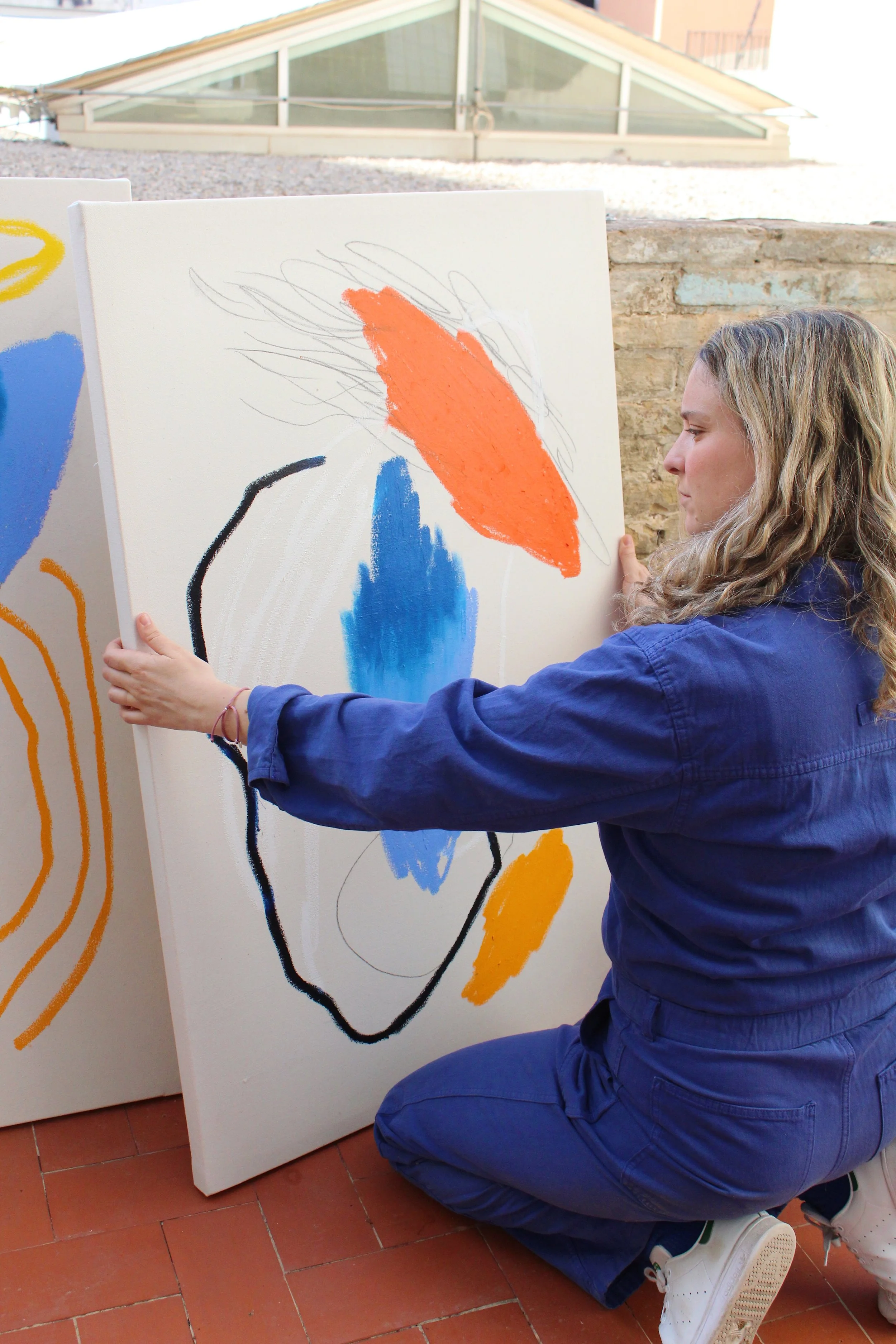 Persona ajustando un cuadro abstracto con colores azul, naranja y negro, vistiendo un traje azul.