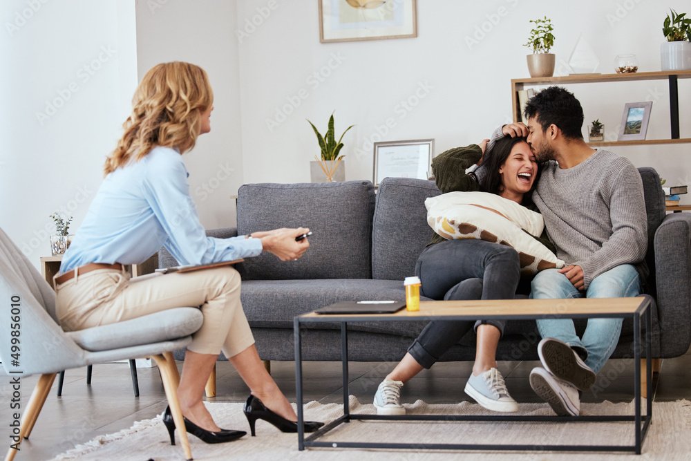 A woman sitting on a chair with a remote in her hand, smelling a couple sitting on a sofa in a cozy living room, with playful and happy expressions