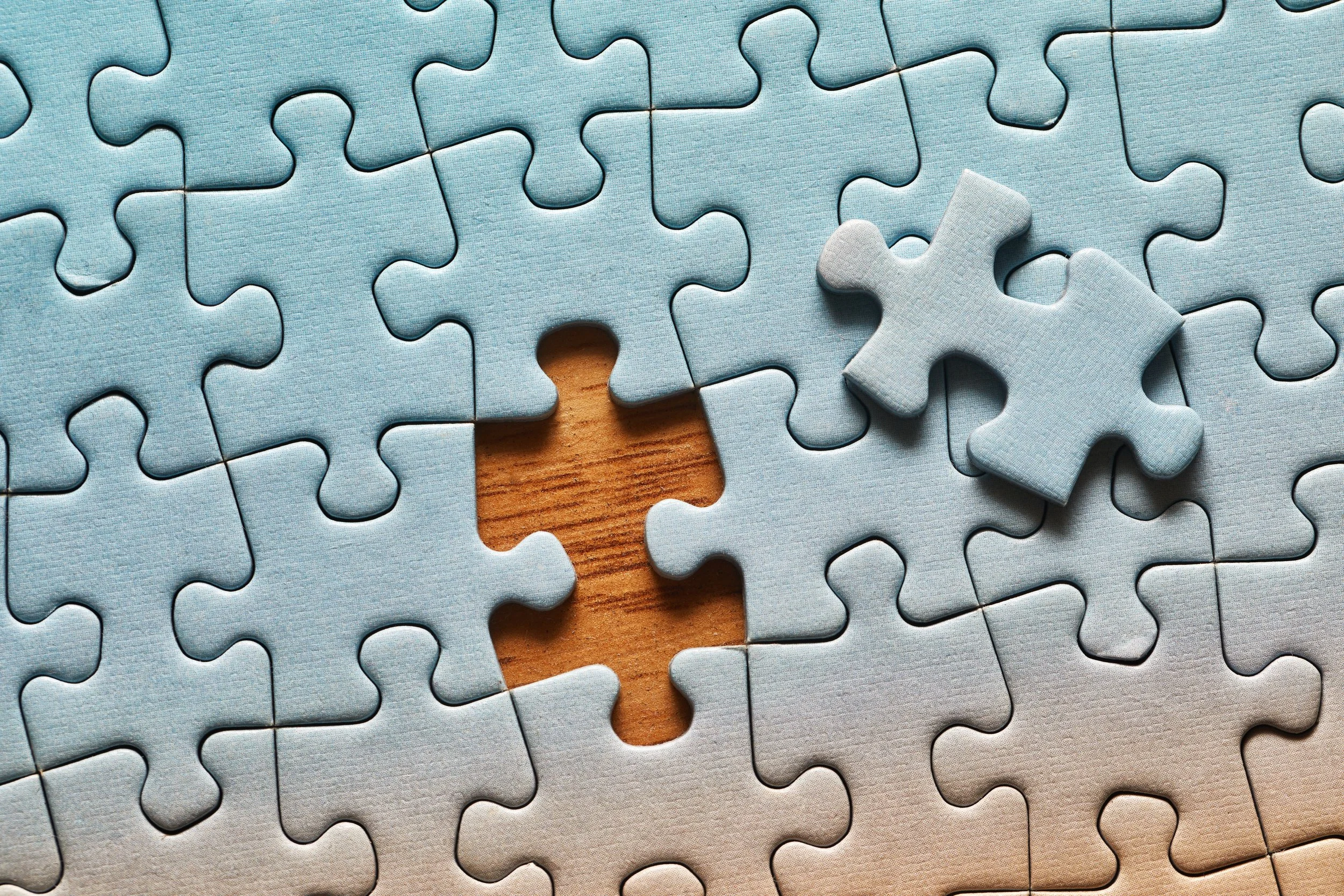 Partial jigsaw puzzle with one missing piece and one piece on top, revealing a wooden surface underneath.