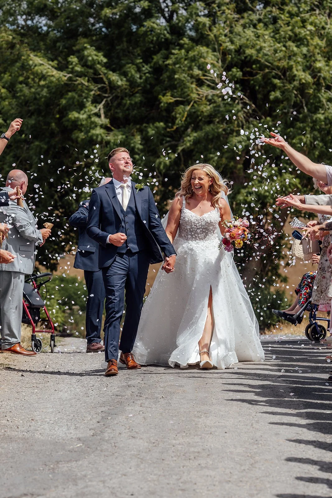 Elise and Tom walking hand in hand through a shower of confetti after their outdoor ceremony at Bowerchalke Barn in Wiltshire, photographed by Just James Weddings.