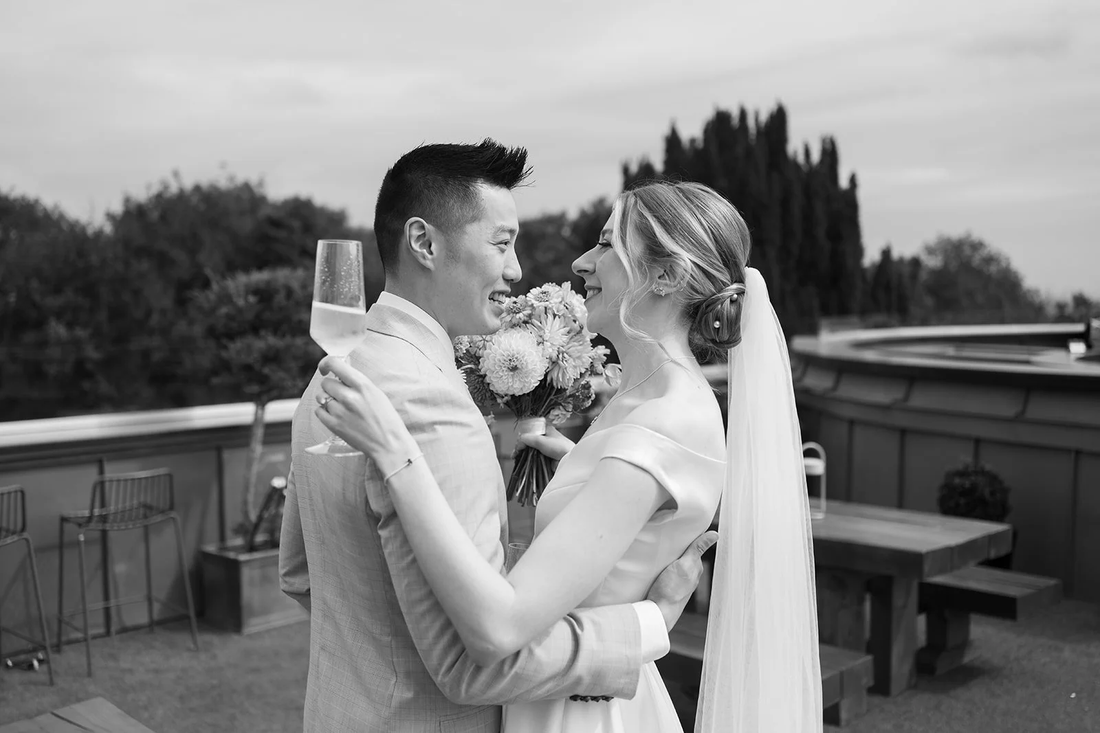 Black and white portrait of Brian & Josie sharing drinks on the terrace at Clifton Observatory in Somerset, photographed by Just James Weddings for relaxed wedding portraits.