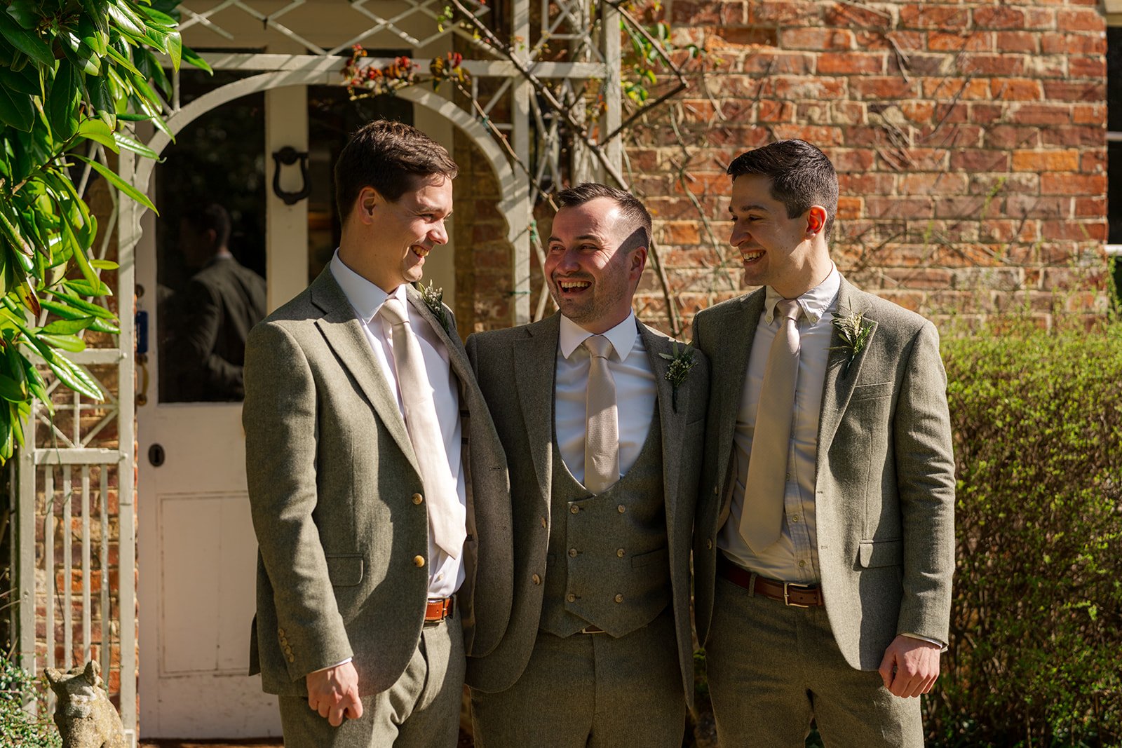 Chris laughs with his groomsmen outside Elmhay Park in Somerset, UK, standing by the brick entrance in matching suits. A warm, joyful portrait from Anna & Chris’s wedding morning, full of friendship, personality, relaxed energy, timeless charm.