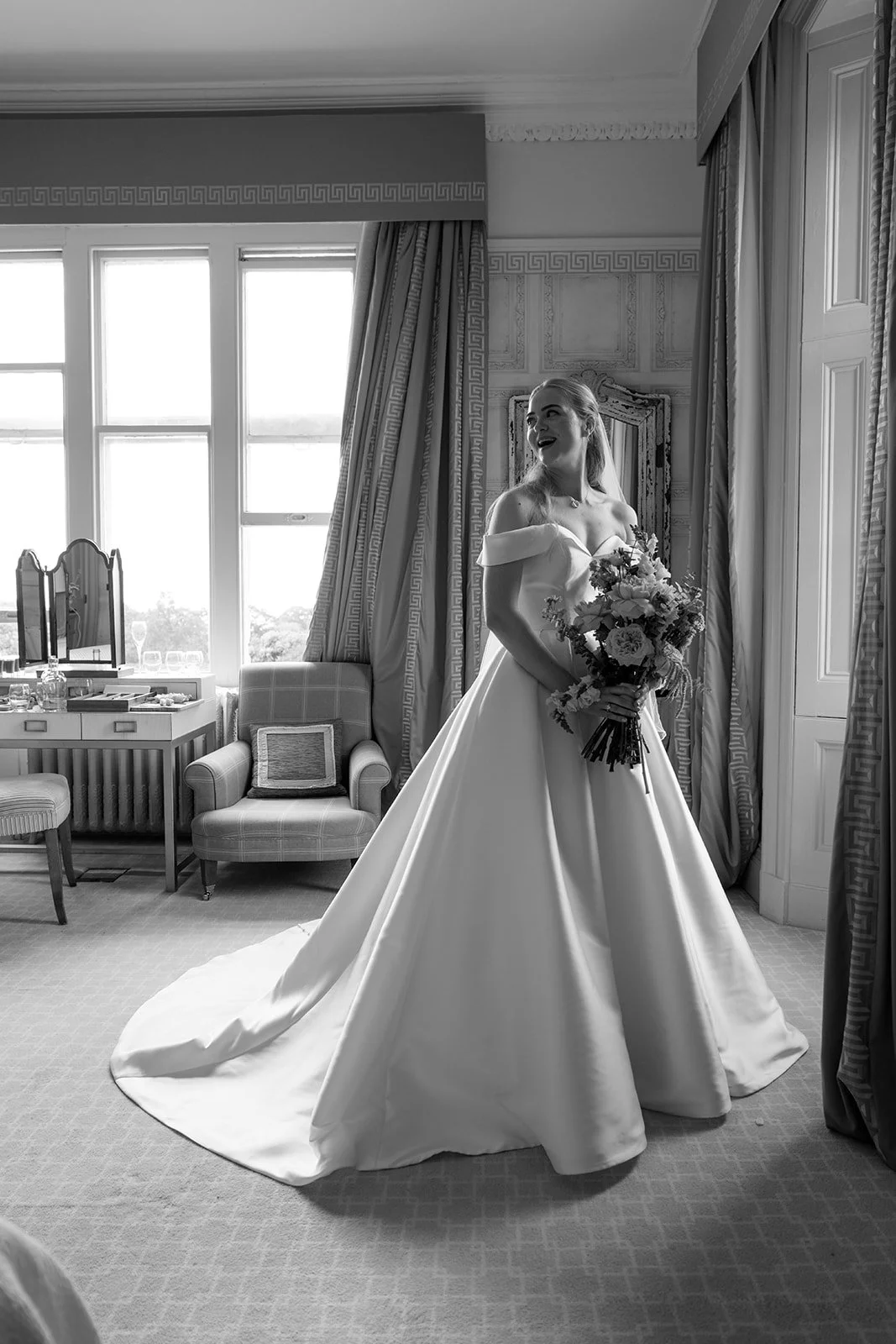 Black and white portrait of Caitlin holding her colourful bridal bouquet in her wedding dress while getting ready at Clevedon Hall in Somerset before marrying Kevin.