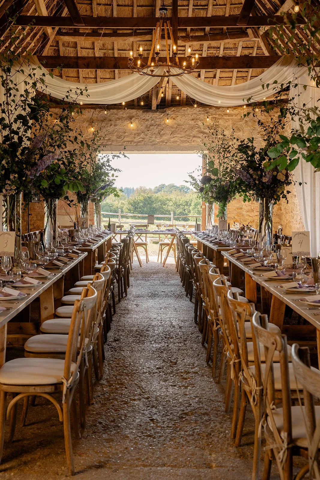 Indoor barn reception at The Cider Barn in Somerset for Abi & Josh’s wedding, with long tables, wooden chairs, floral arrangements, draped fabric and countryside views, photographed by Just James Weddings for rustic wedding venue.