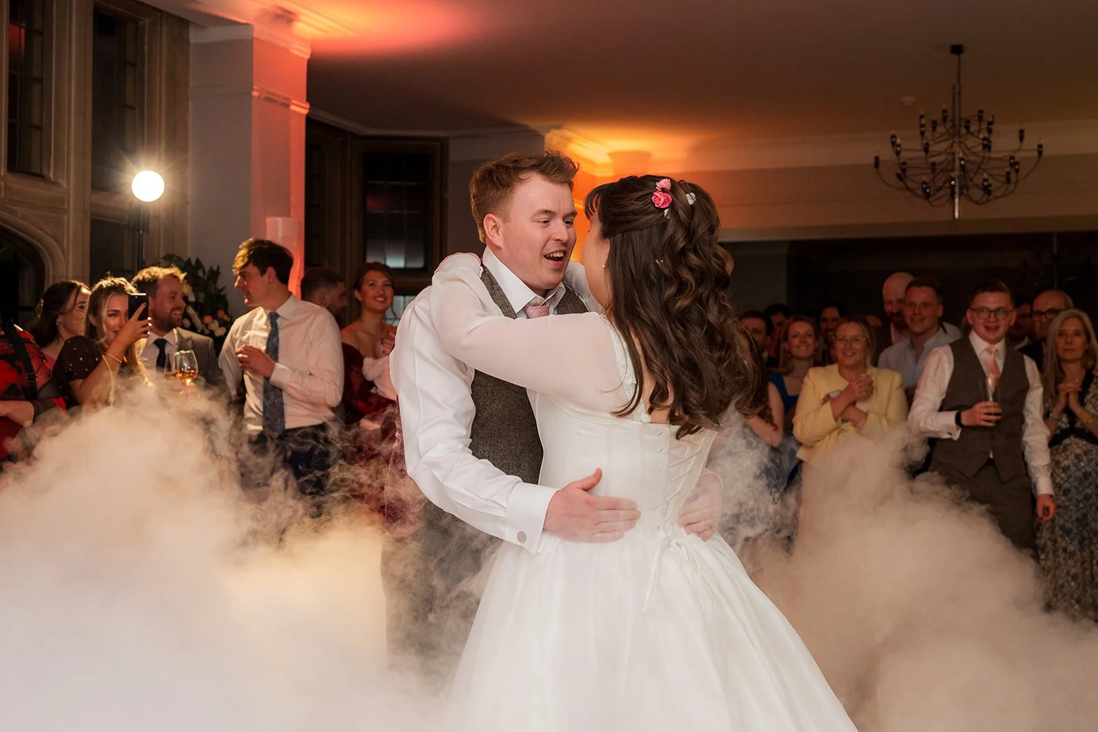 Emily and Josh share their first dance at Coombe Lodge in Somerset, UK, surrounded by guests and dramatic low-lying smoke during their evening wedding celebration.